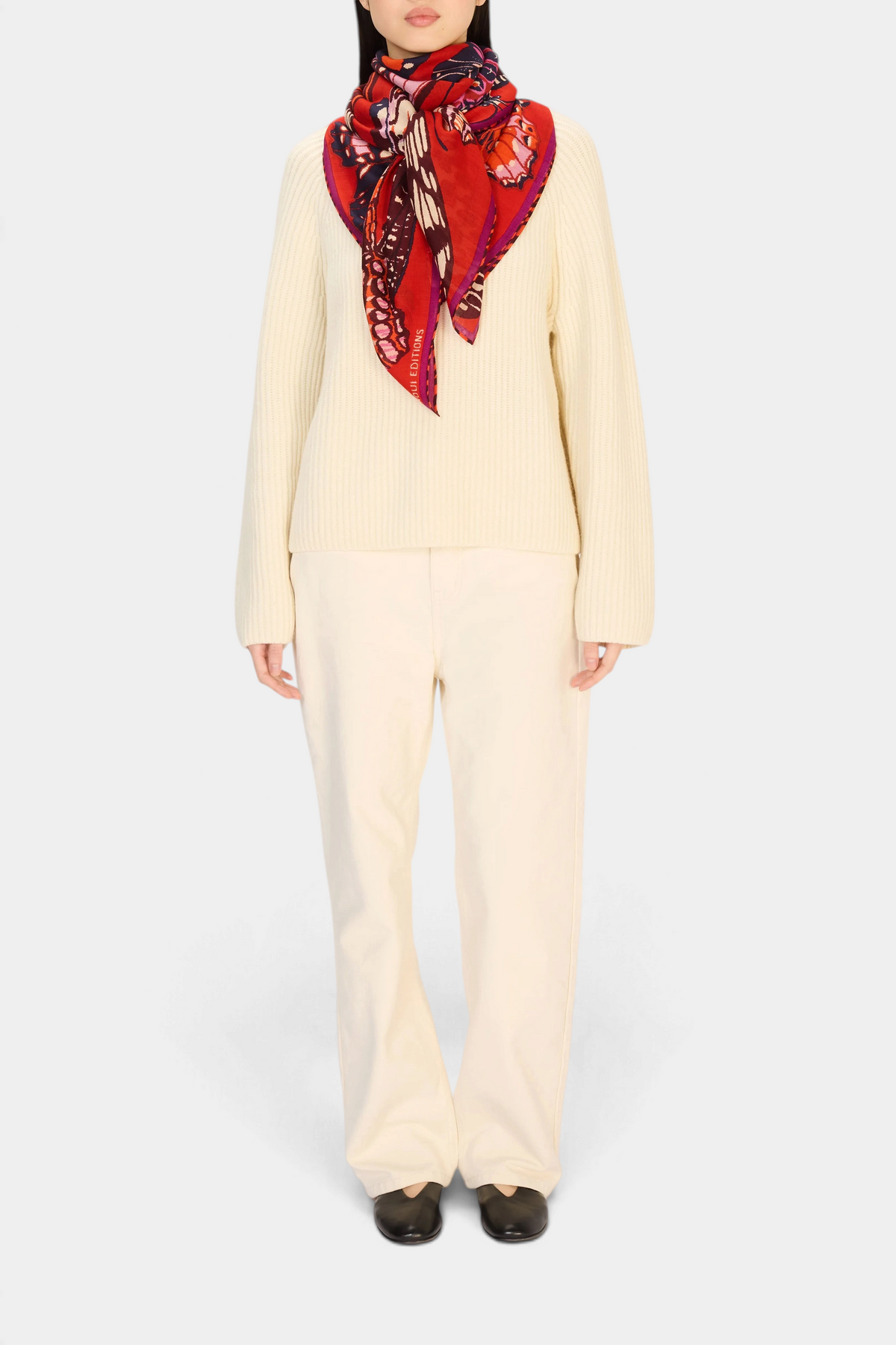 Model wearing The Copper Shed Square 130 Papillons red wool scarf with butterfly print over a cream sweater and pants