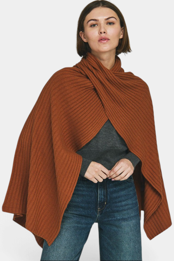 The Copper Shed rust orange ribbed knit cape with a funnel neckline and handkerchief hem worn by a woman.