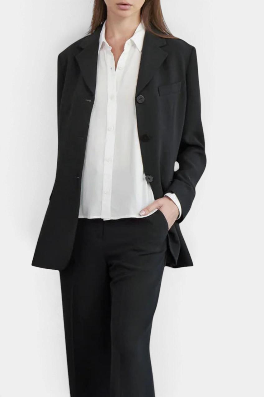 The Copper Shed Stacey blouse in white rayon crepe with button cuffs, worn under a black blazer.