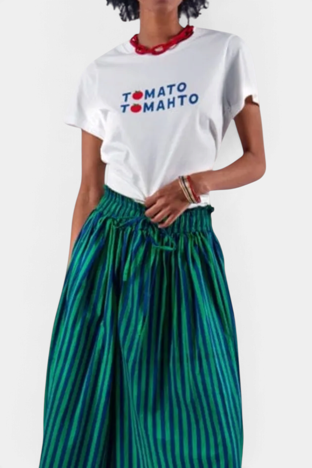 The Copper Shed white graphic t-shirt with Tomato Tomahto text print worn by a model with a green striped skirt