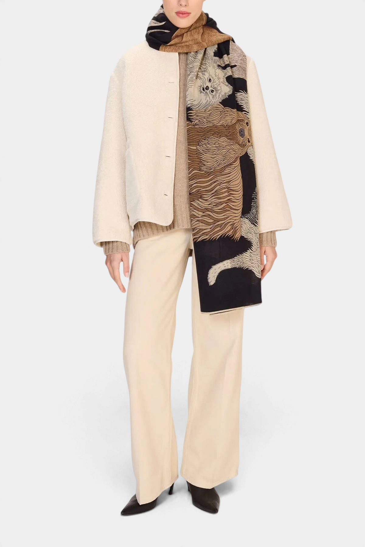 The Copper Shed Toutou wool scarf in black with a tan dog pattern worn by a model in a cream jacket and trousers