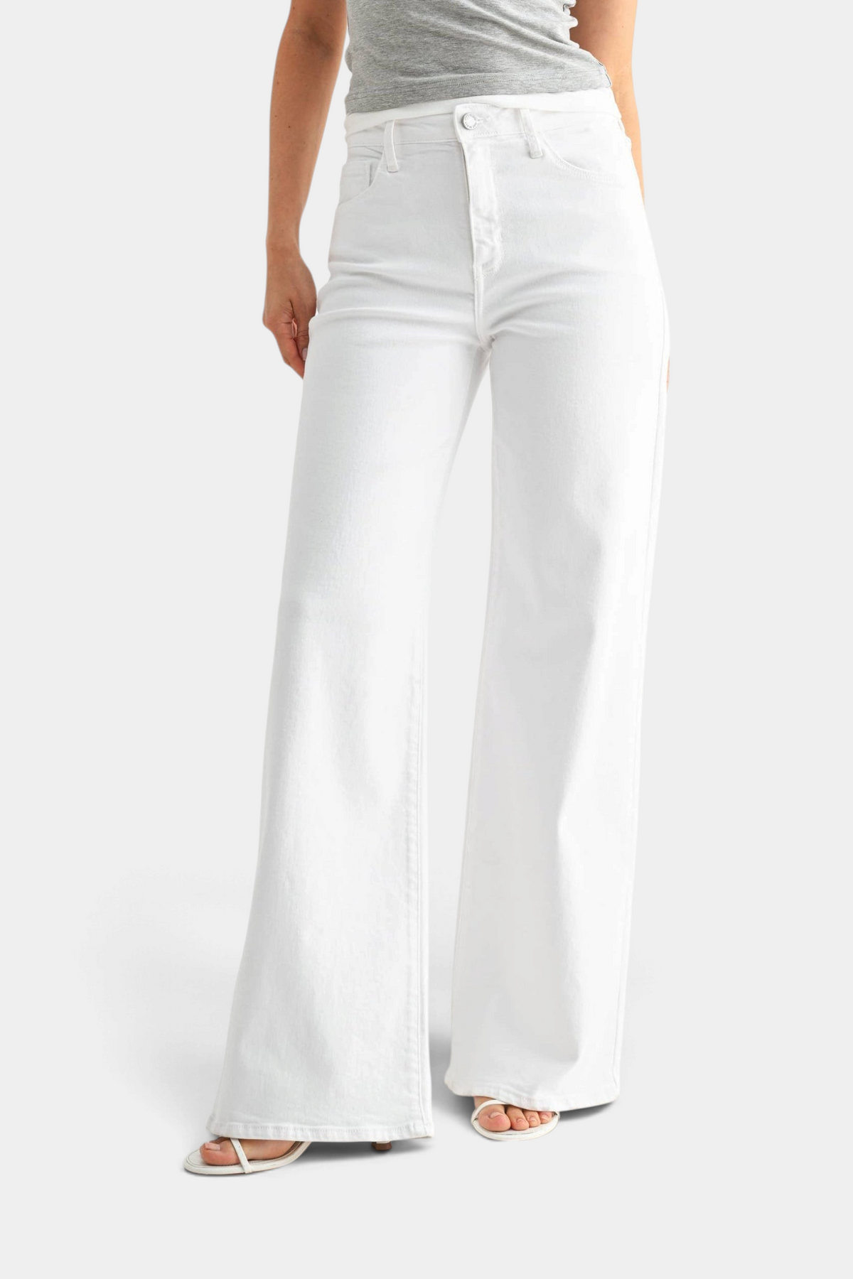 The Copper Shed white stretchy wide leg jeans worn by a model with a grey top and white strappy sandals.