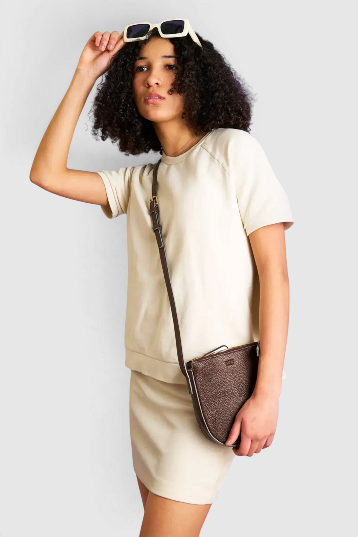 The Copper Shed Yash small crossbody bag in dark brown pebble grain Italian leather worn by a model in a beige outfit