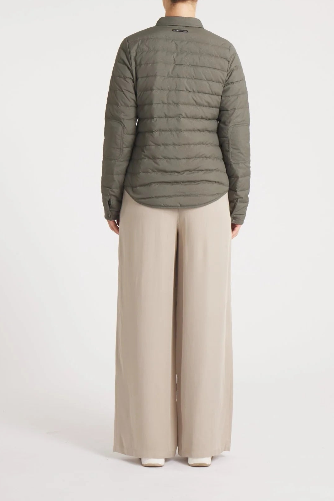 Person wearing a green puffer jacket and beige pants on a white background