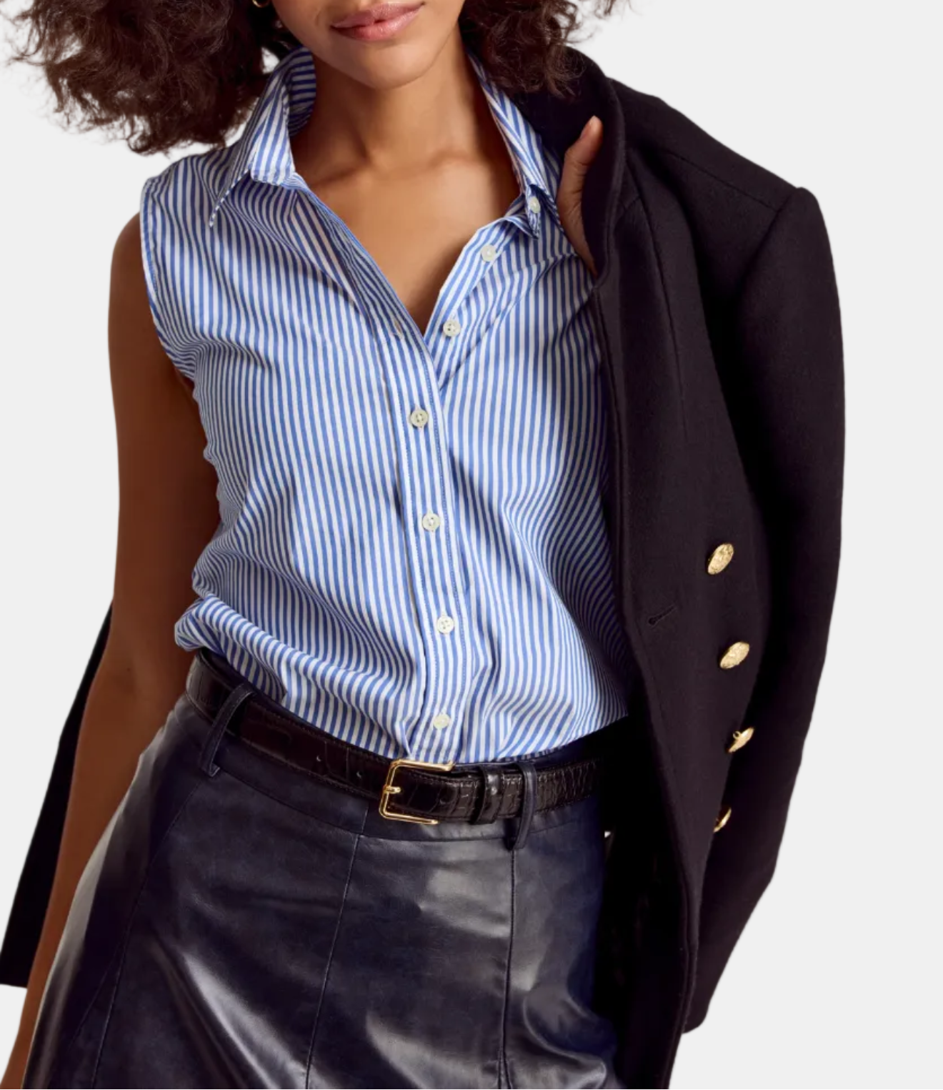 A woman wearing a sleeveless striped shirt in blue and white, with a black jacket draped over the shoulders and a leather skirt.