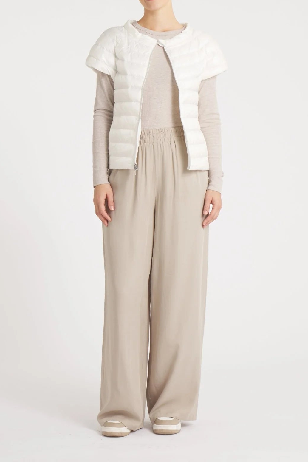 Woman wearing a light gray cardigan over a white top and beige pants on a white background