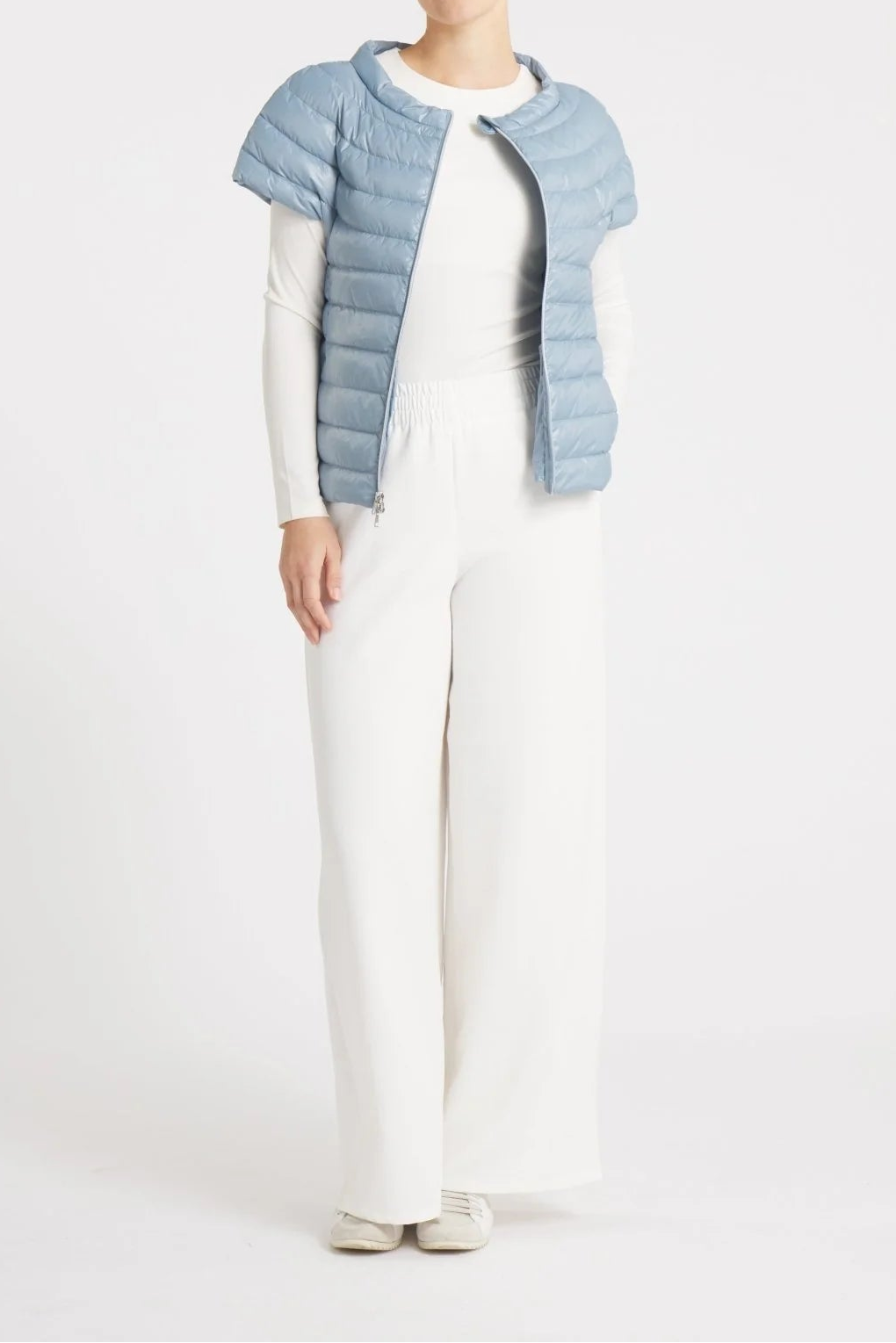 Person wearing a light blue quilted vest over a white outfit on a white background