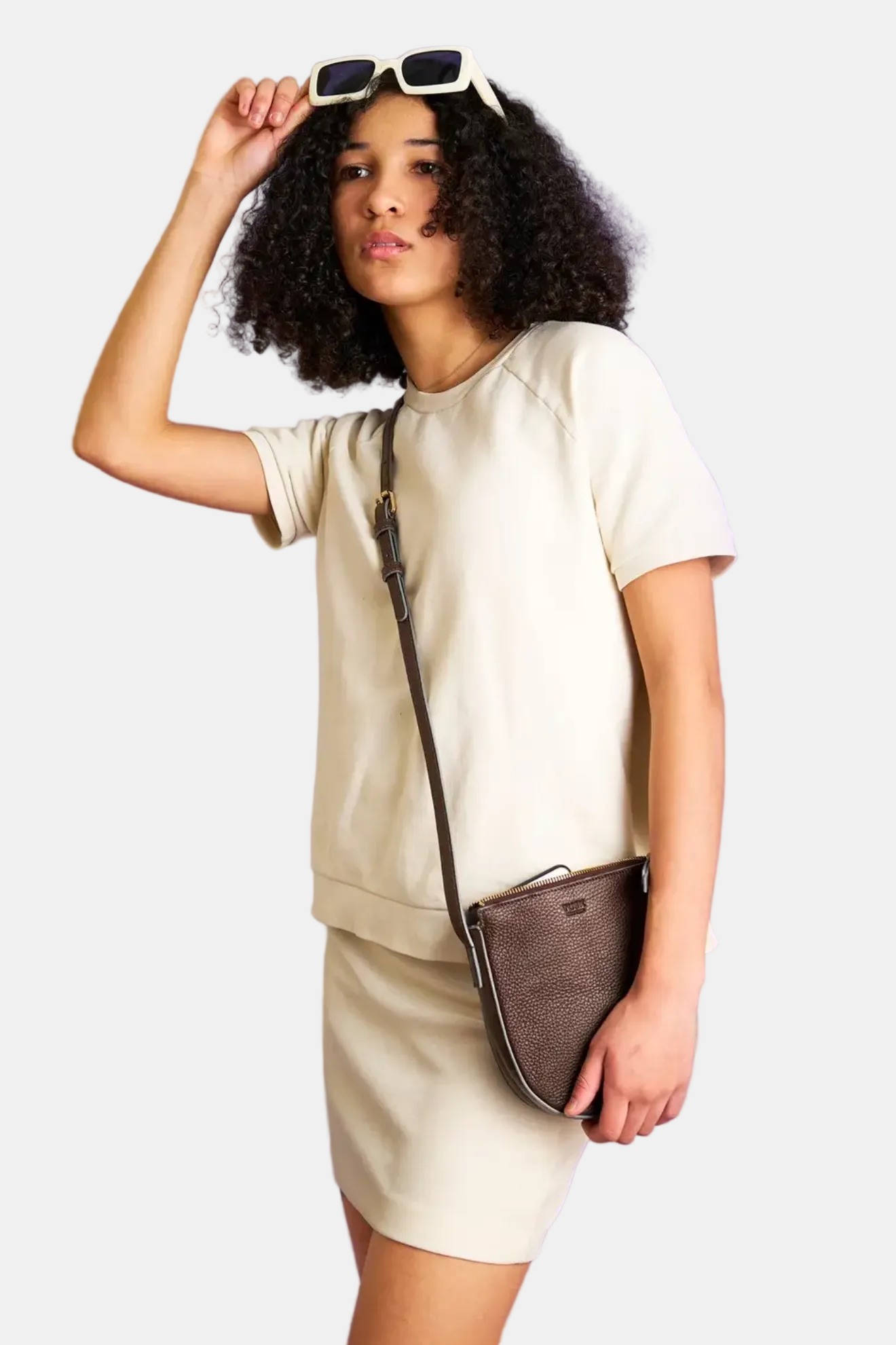 Woman holding sunglasses and a brown handbag against a purple background