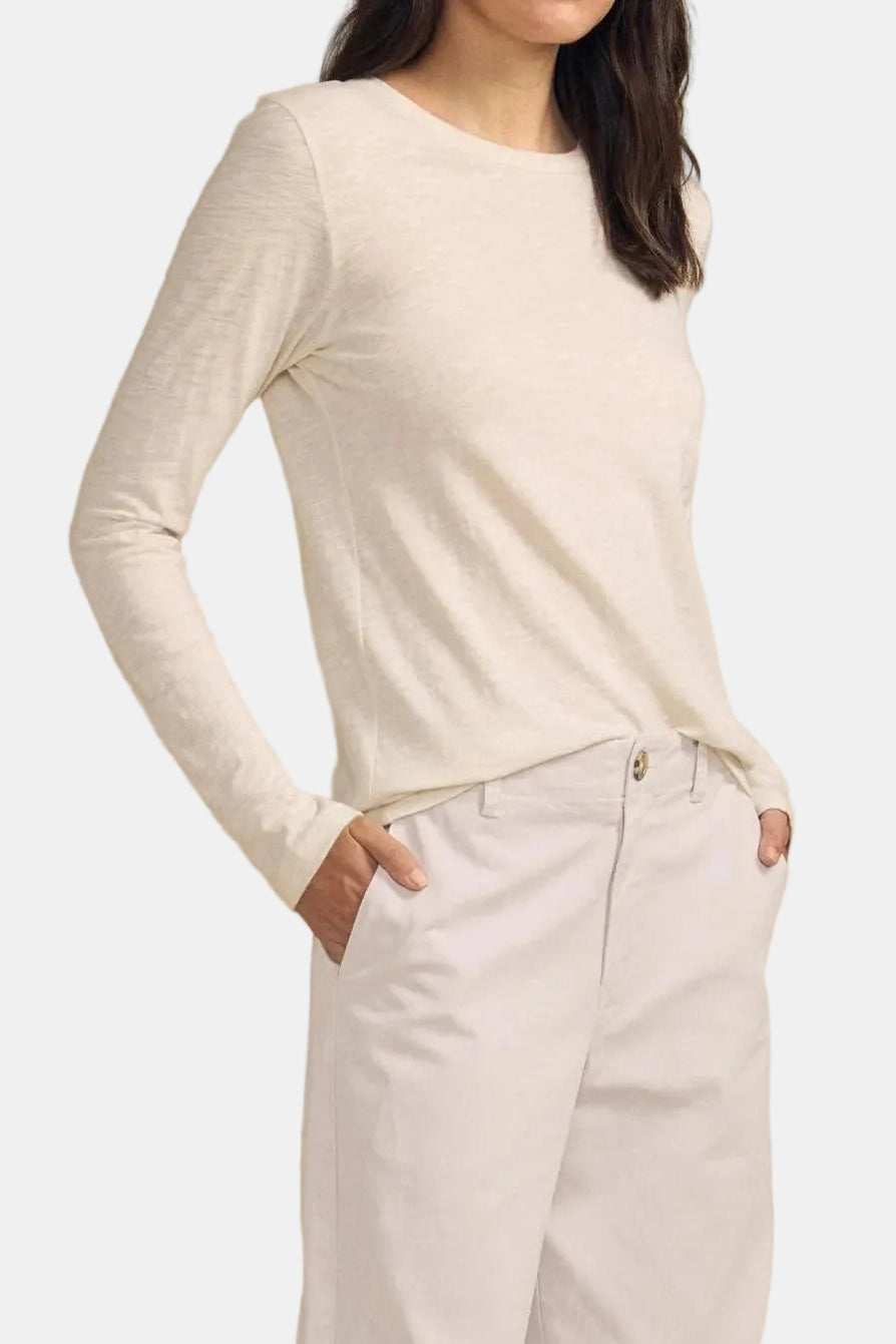 A woman modeling a cream-colored long-sleeve knit top and matching light trousers against a solid beige studio background.