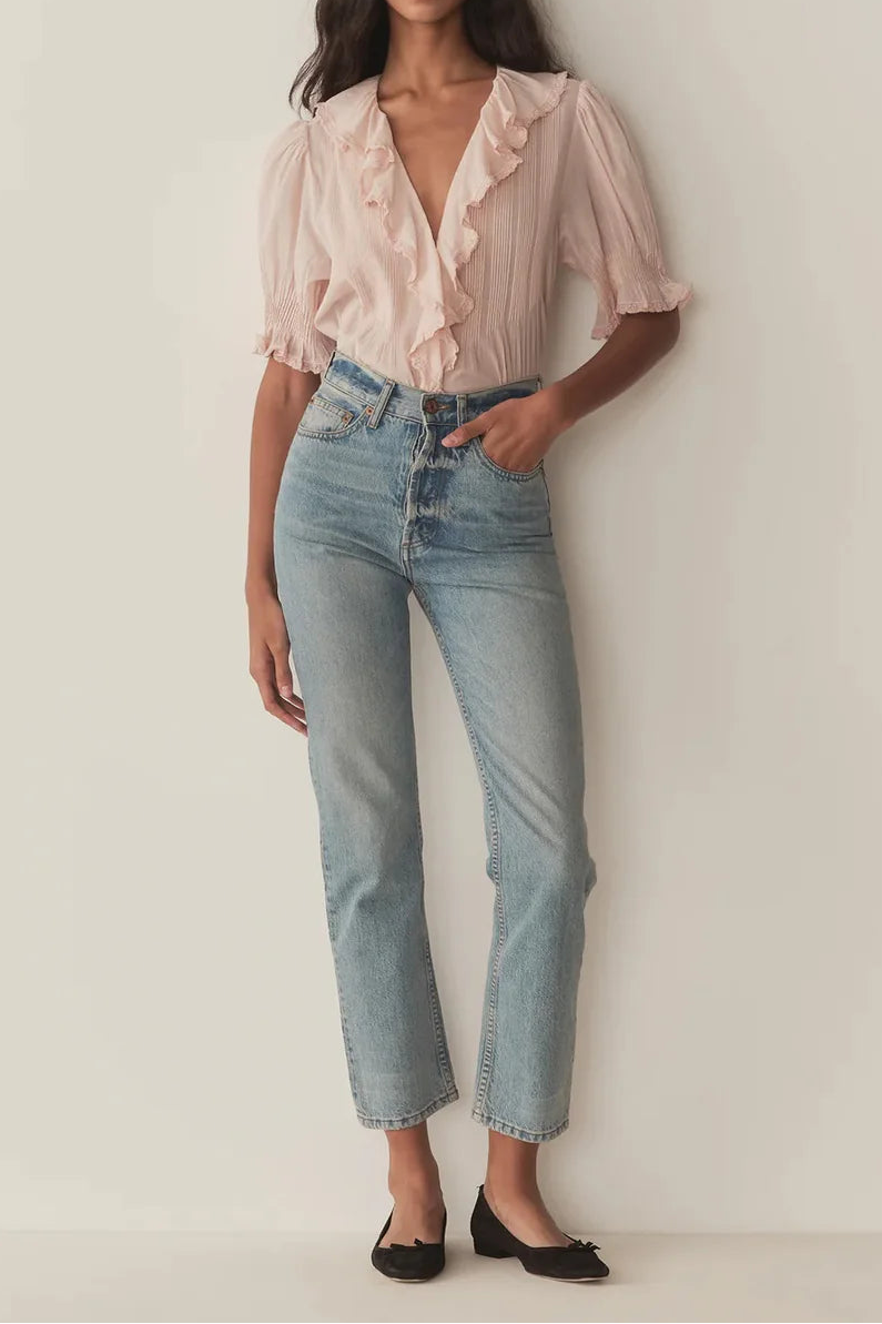 Woman wearing a light pink blouse and blue jeans against a white background