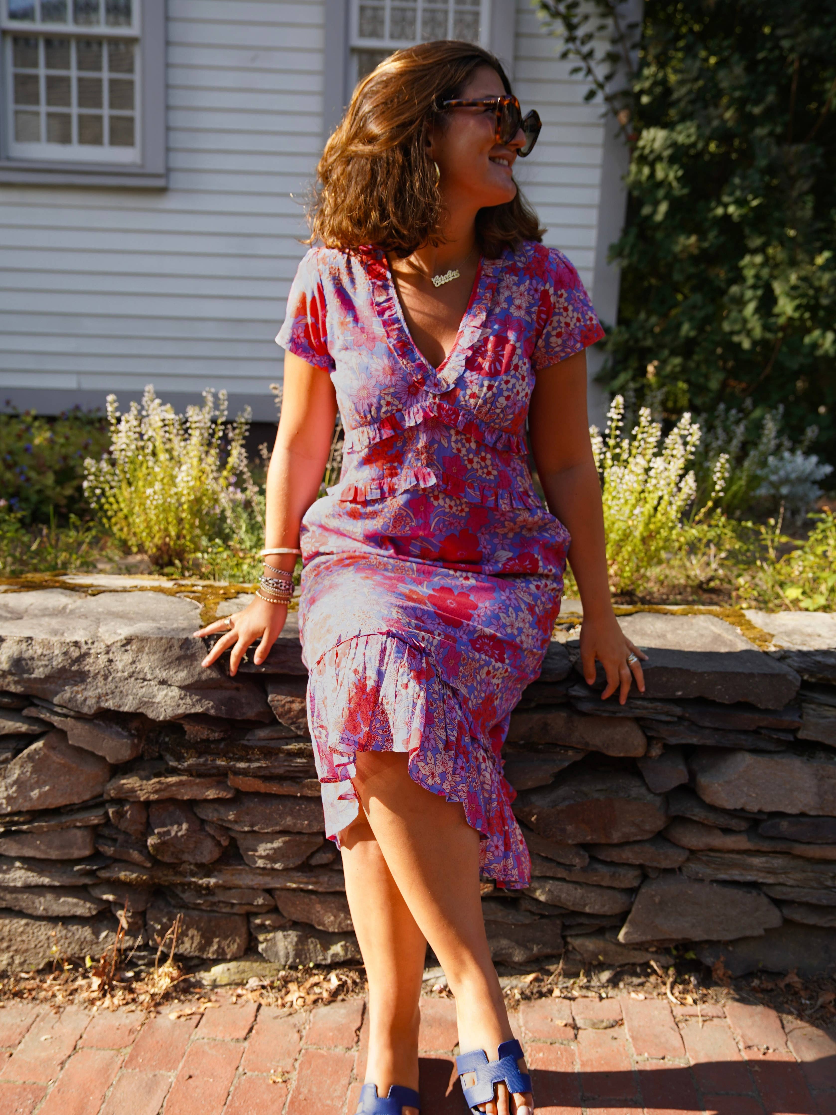 Woman in a colorful dress standing outdoors near a stone wall.