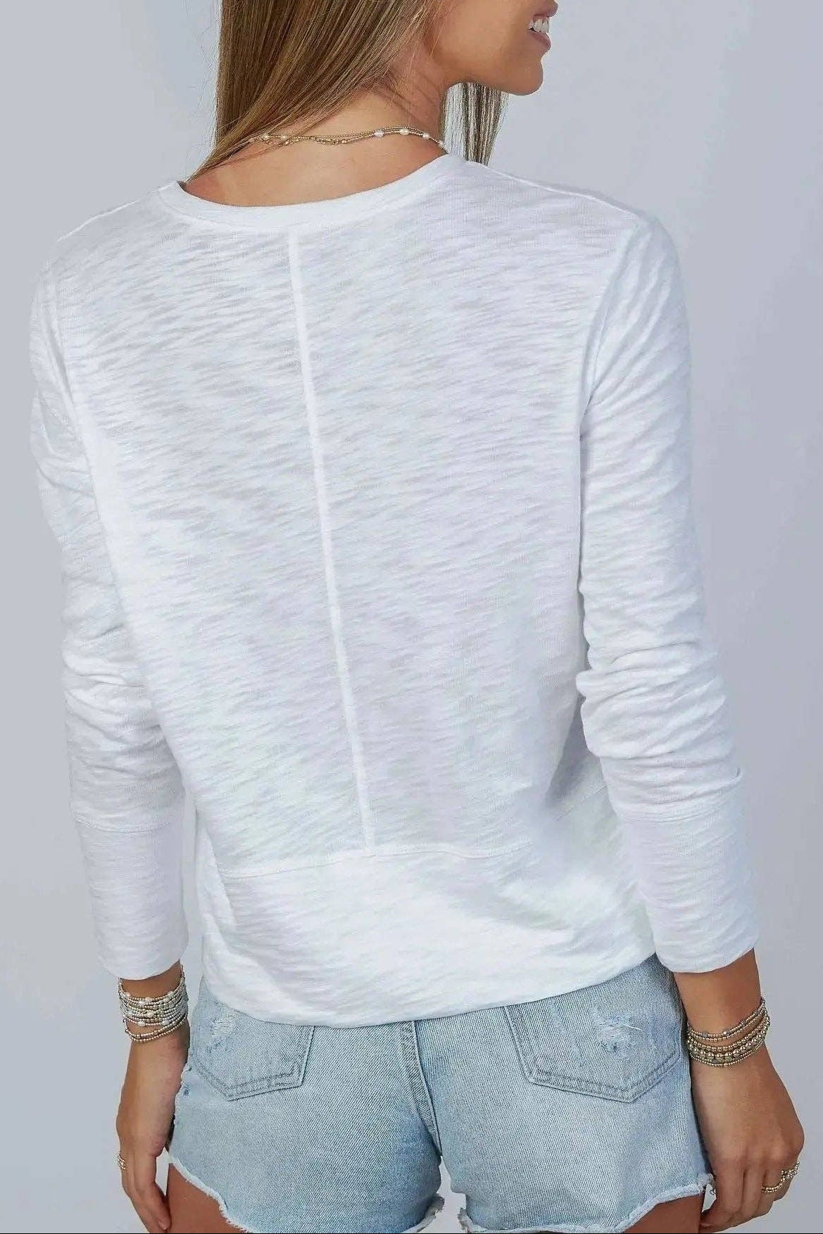Woman wearing a white long-sleeve top and denim shorts against a plain background