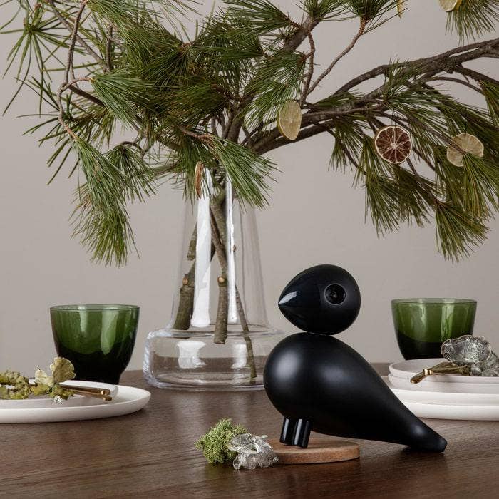 Decorative black bird sculpture on a wooden table with greenery and candles in the background.