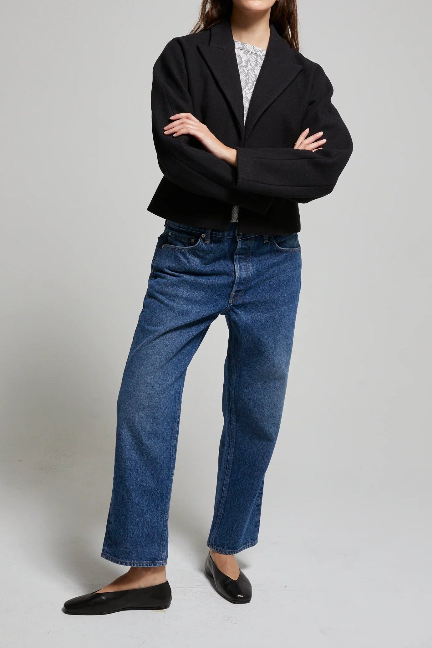 Person wearing a black blazer and blue jeans on a plain background