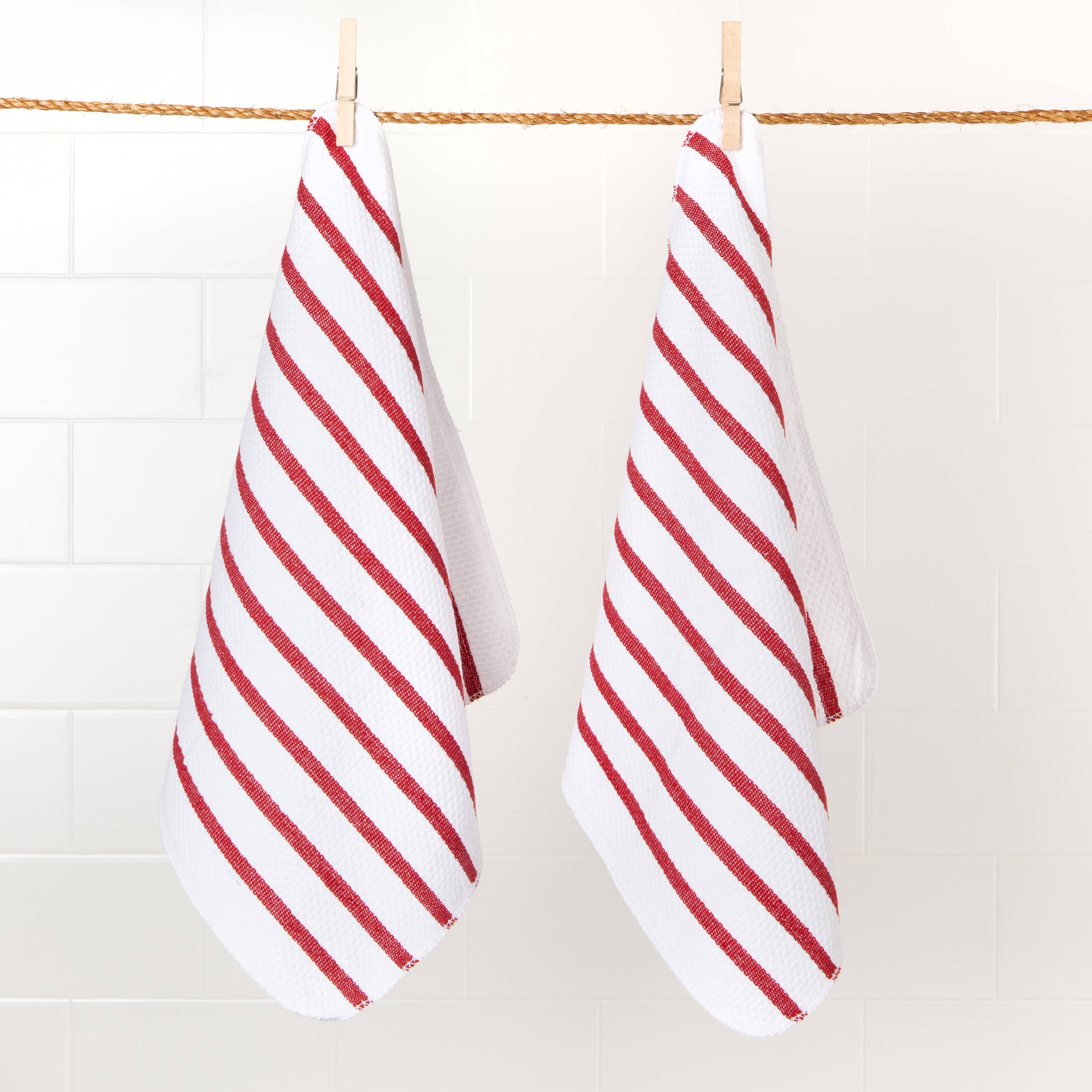 Two red and white striped towels hanging on a line against a tiled wall.