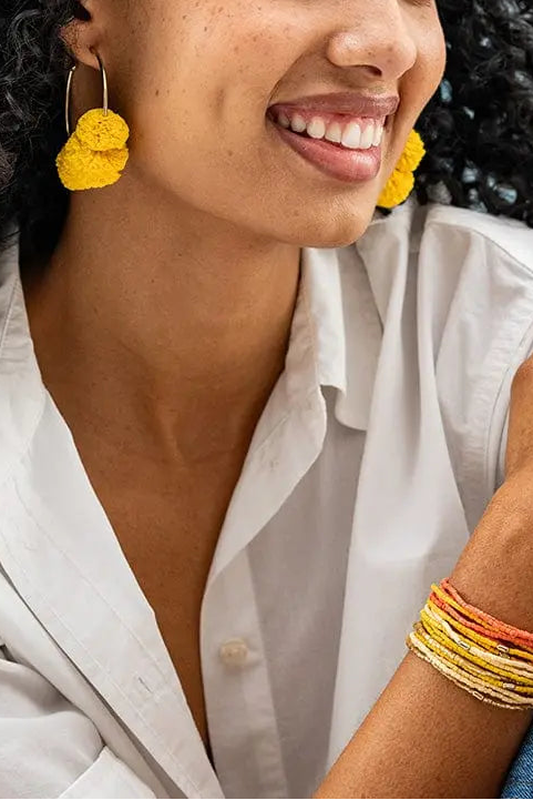 Woman wearing yellow earrings and colorful bracelets against a light blue background