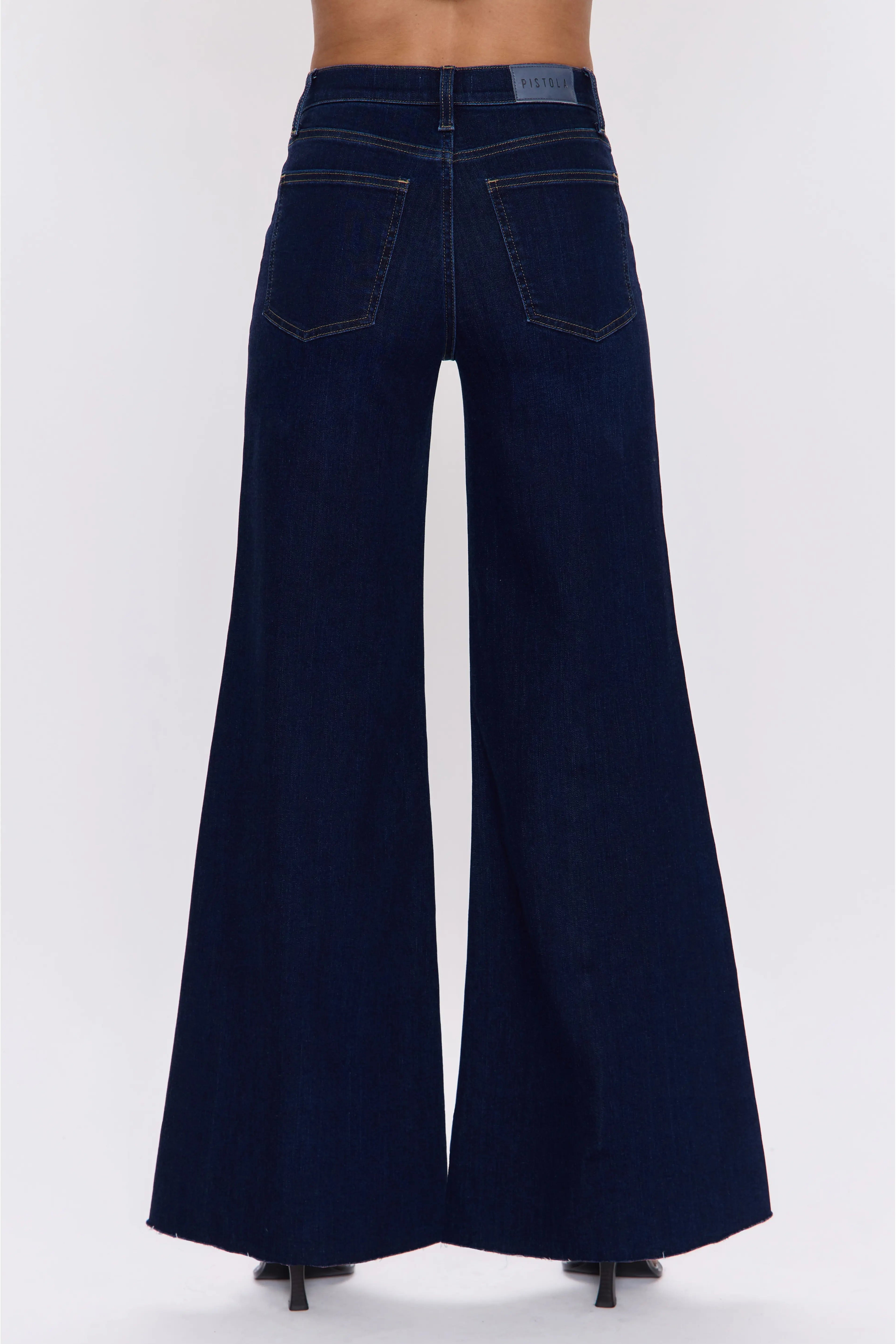 Rear view of a model wearing dark navy blue wide-leg denim jeans with a high waist and back pockets, shown against a plain light gray studio background.
