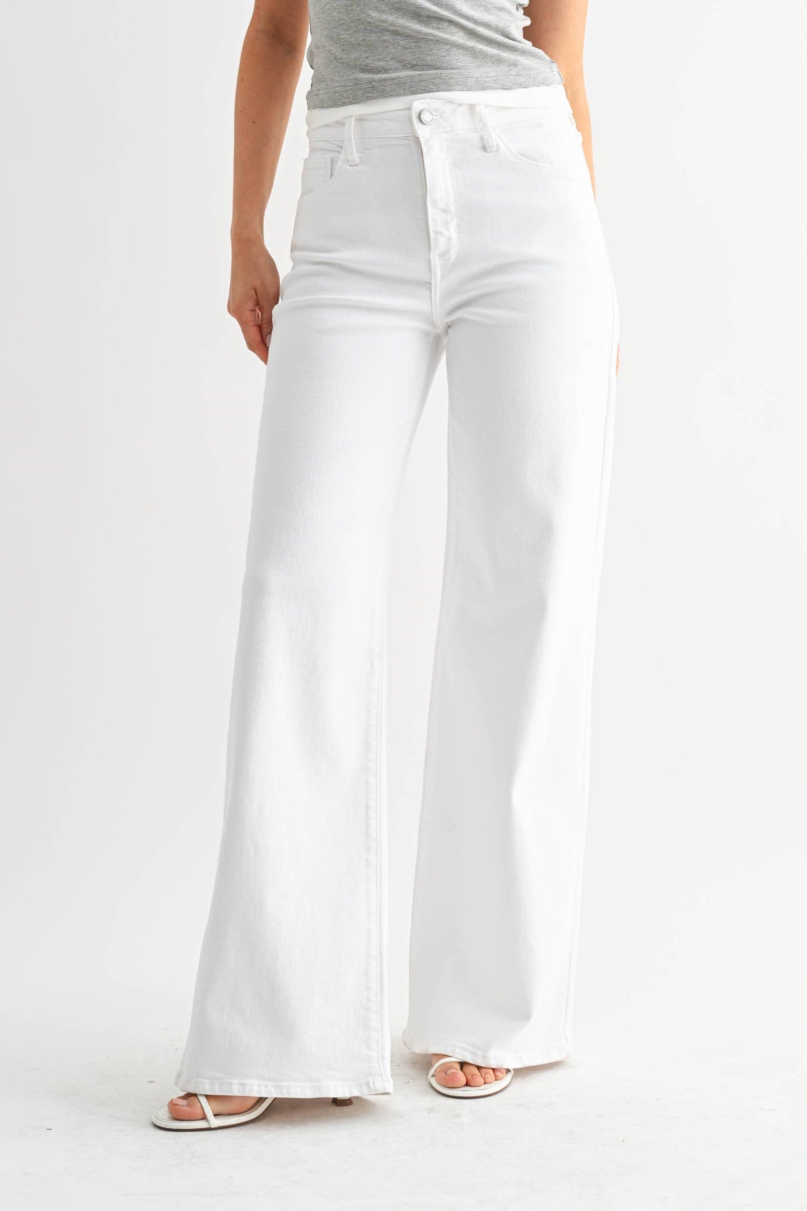 Woman wearing a gray off-shoulder top and white wide-leg pants on a white background