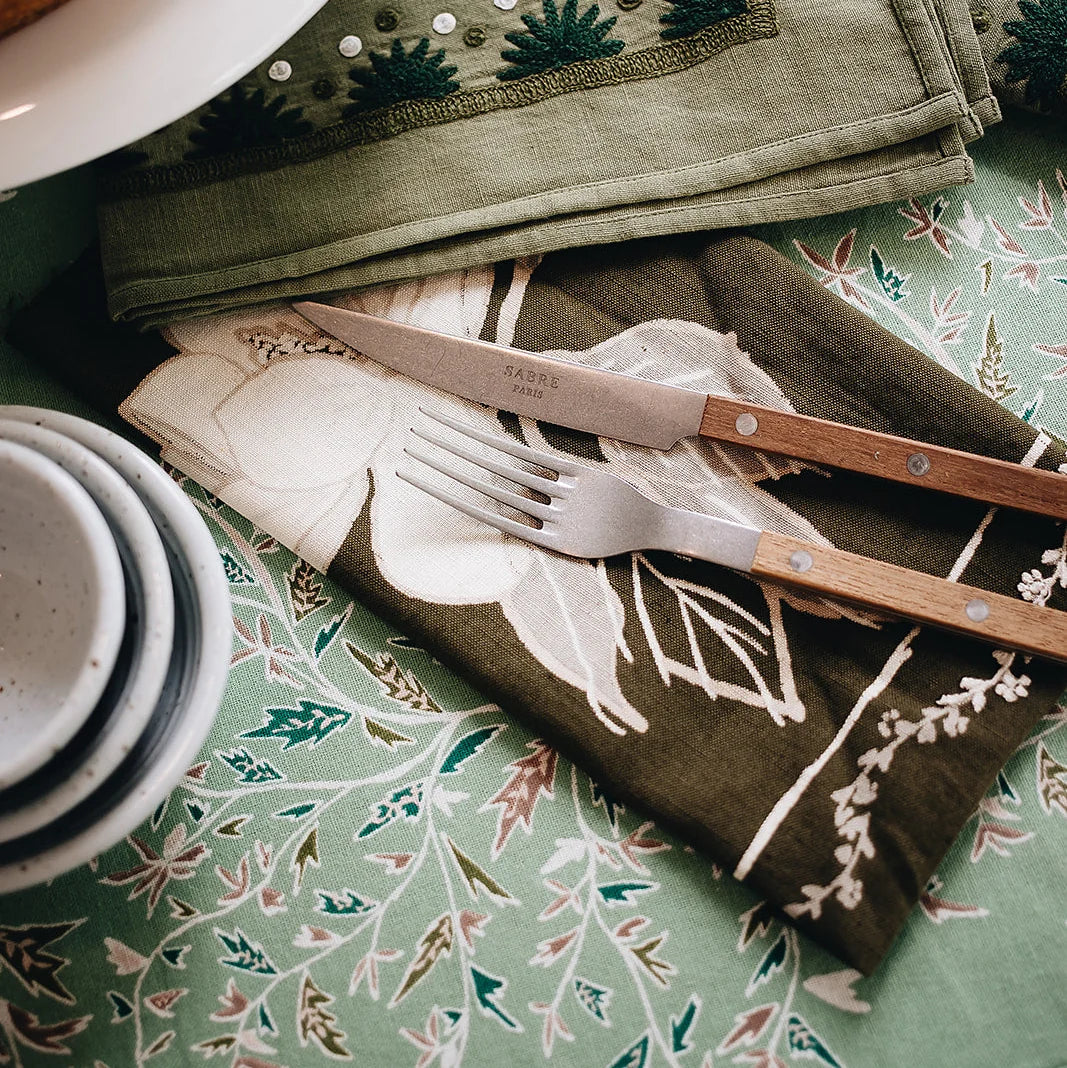 Set of cutlery on a patterned tablecloth with a green and white floral design.