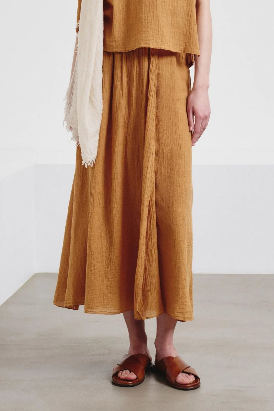 Woman wearing a mustard yellow top and skirt with a white scarf, standing against a plain background.