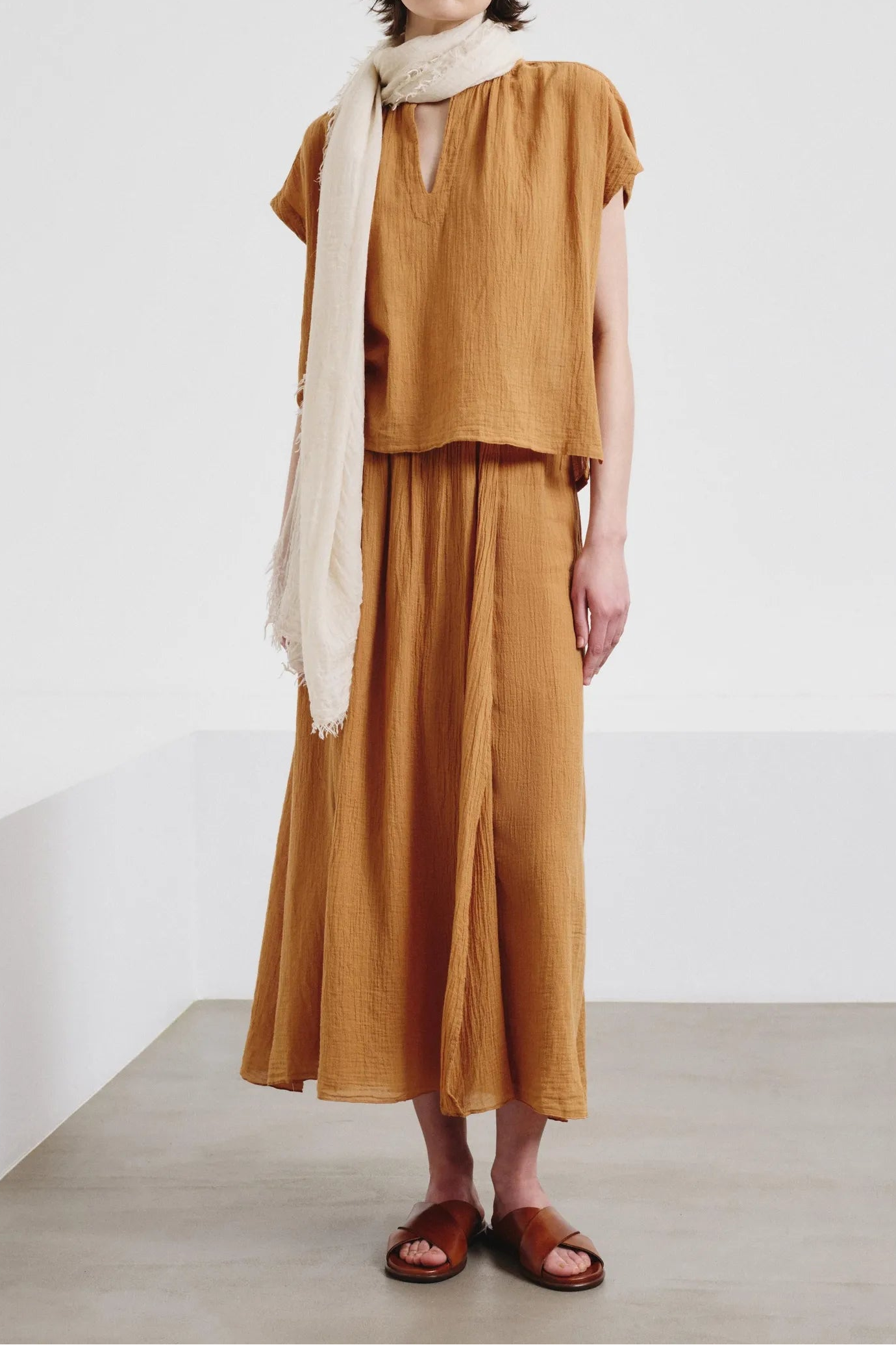 Woman wearing a mustard yellow top and skirt with a white scarf, standing against a plain background.