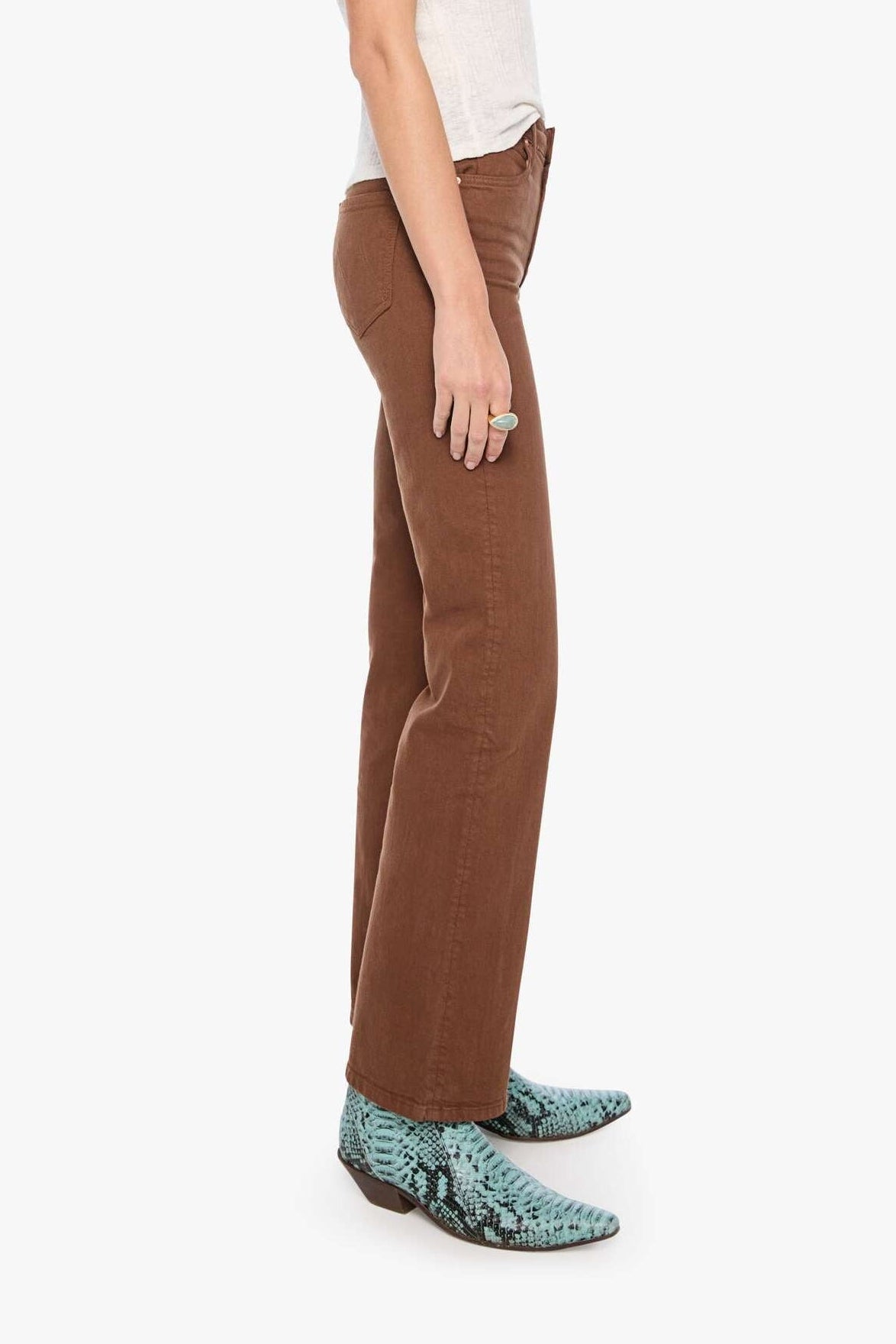 Woman wearing a white sleeveless top, brown pants, and turquoise cowboy boots on a white background
