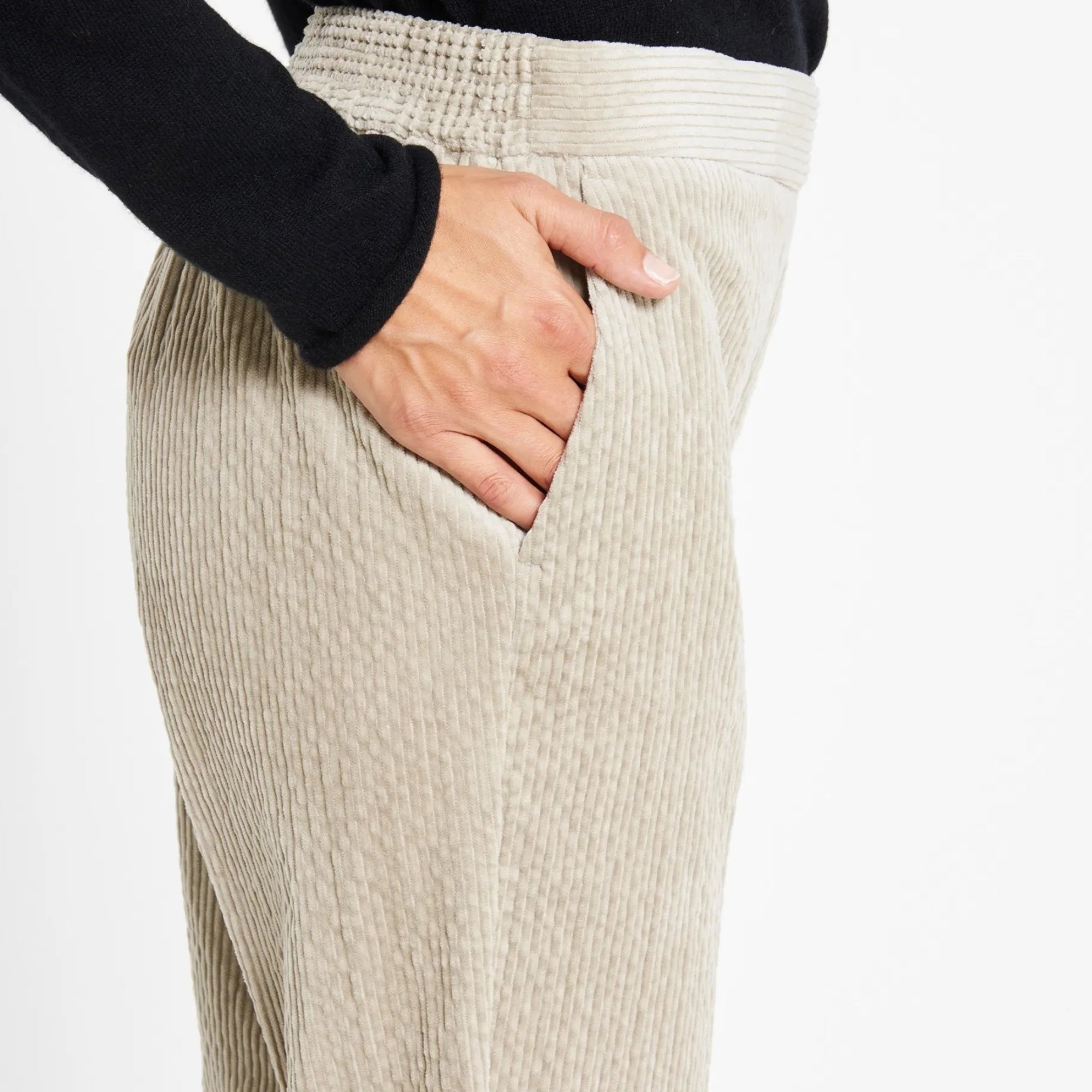 Close-up of a person wearing light beige corduroy pants with a black long-sleeve top, showing the side pocket and hand.