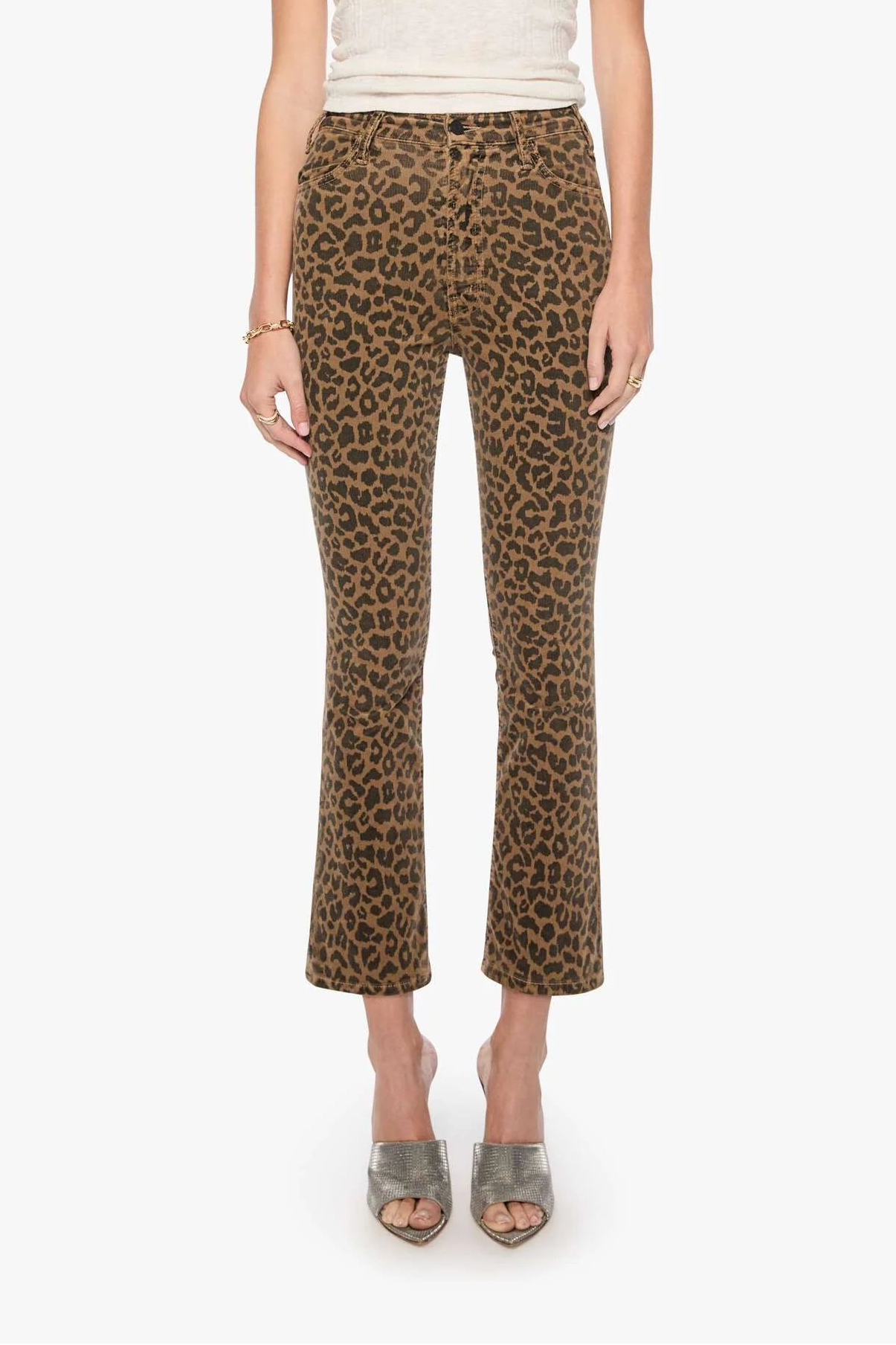 A woman modeling a pair of brown leopard-print cropped pants with a cream short-sleeve top, standing against a plain light gray background.