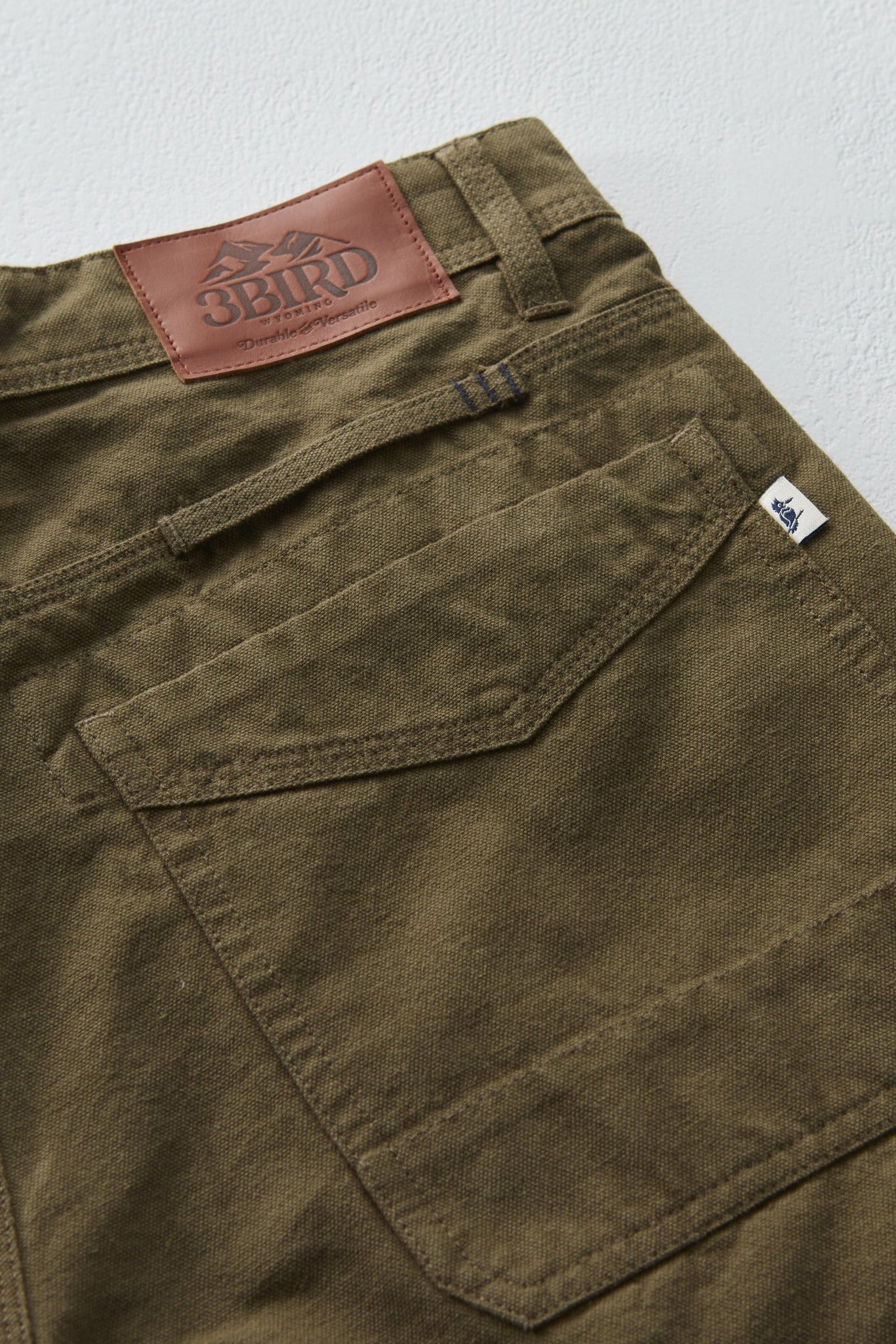 Close-up of olive green pants with a brand label on a light gray background