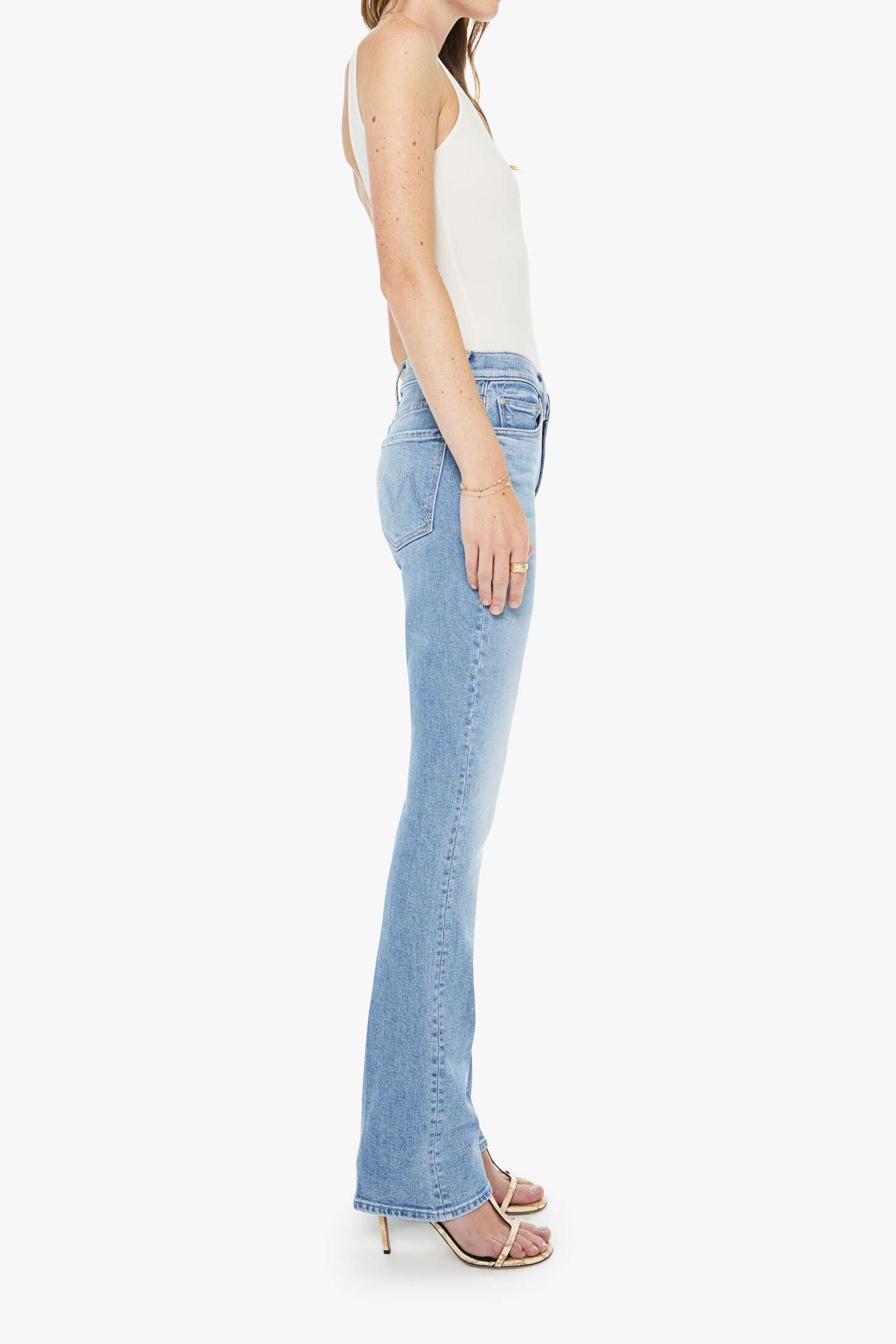 Woman wearing light blue flared jeans and a white top on a white background
