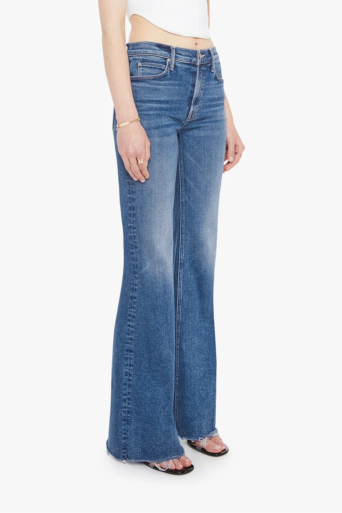 A model wearing blue high-waisted flare jeans with a faded wash, styled with a white crop top and clear-strap sandals against a plain white background.