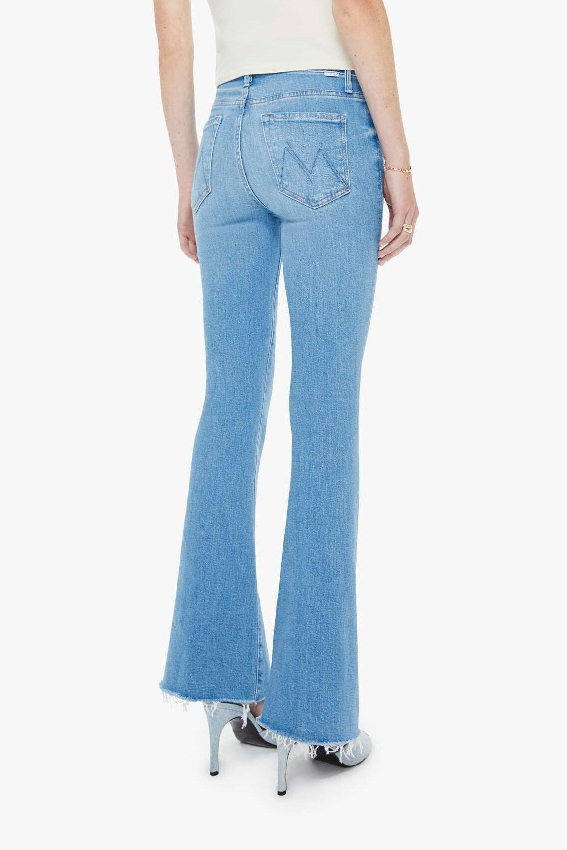 Woman wearing light blue flared jeans and a white top on a white background