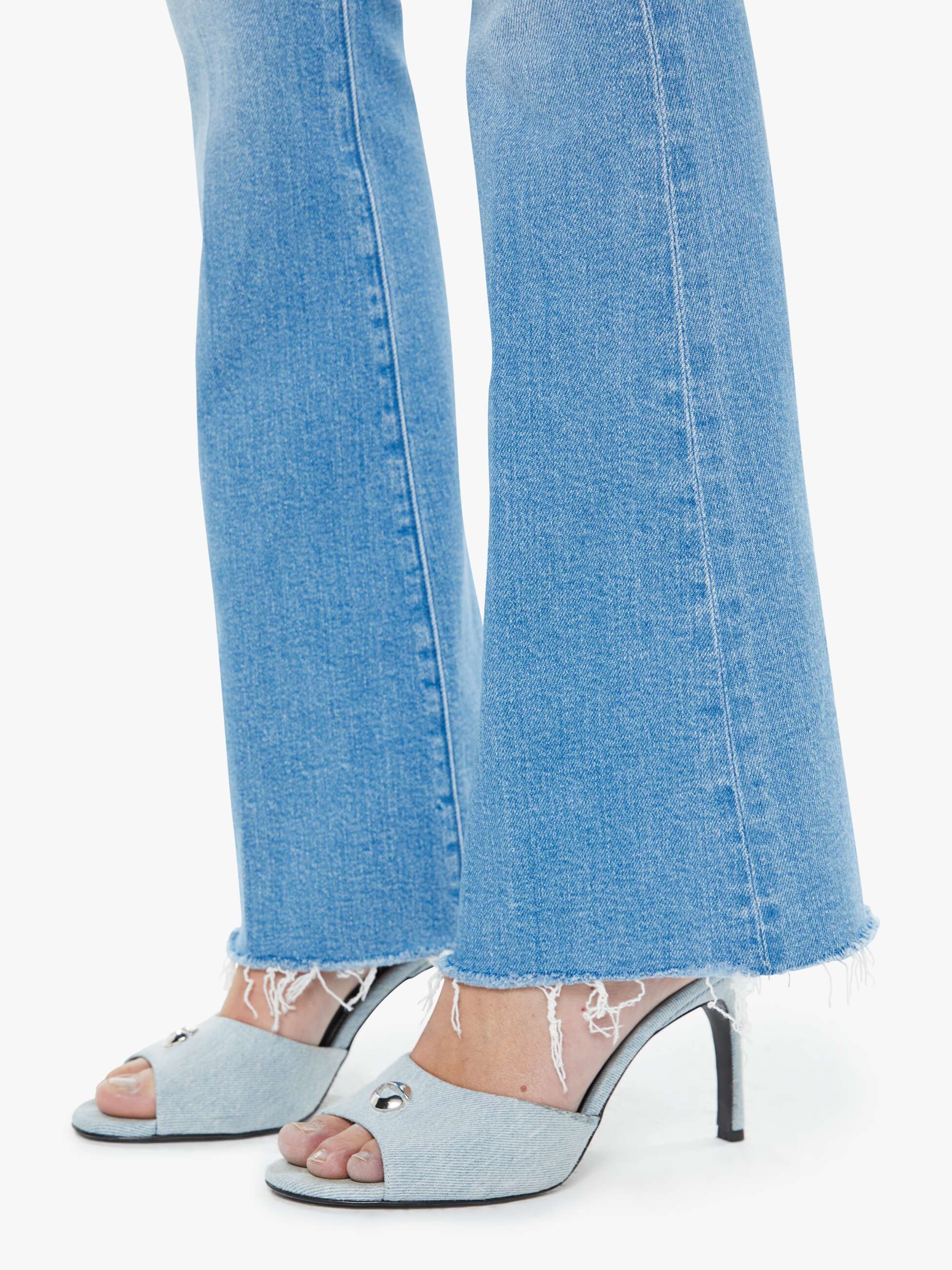Light blue denim jeans with silver open-toe high-heeled shoes on a white background