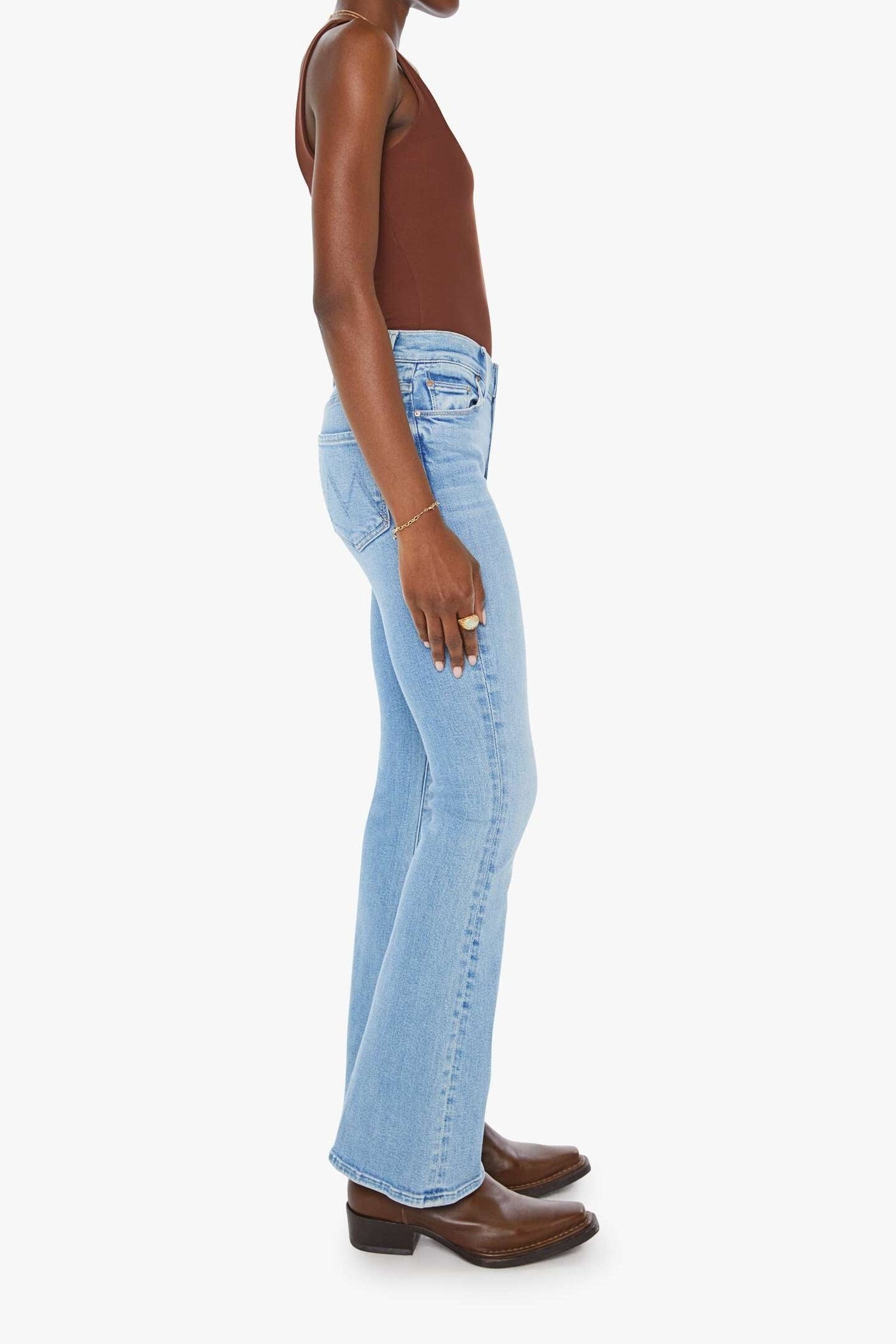 Woman wearing light blue jeans and a brown top on a white background