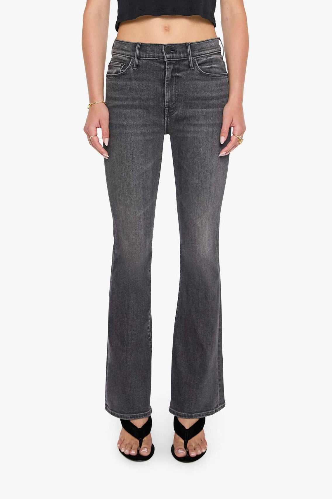 Woman wearing a black crop top and gray flared jeans on a white background