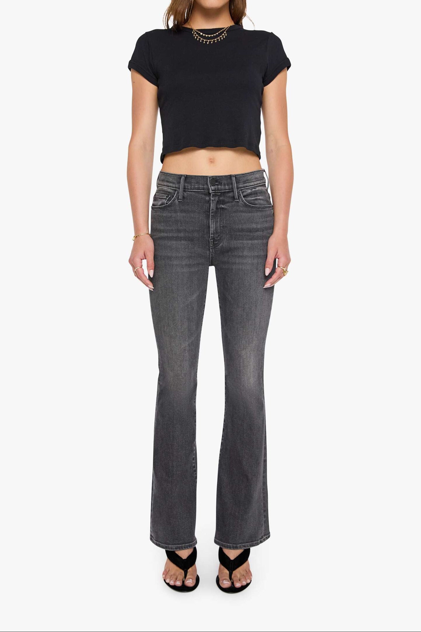 Woman wearing a black crop top and gray flared jeans on a white background