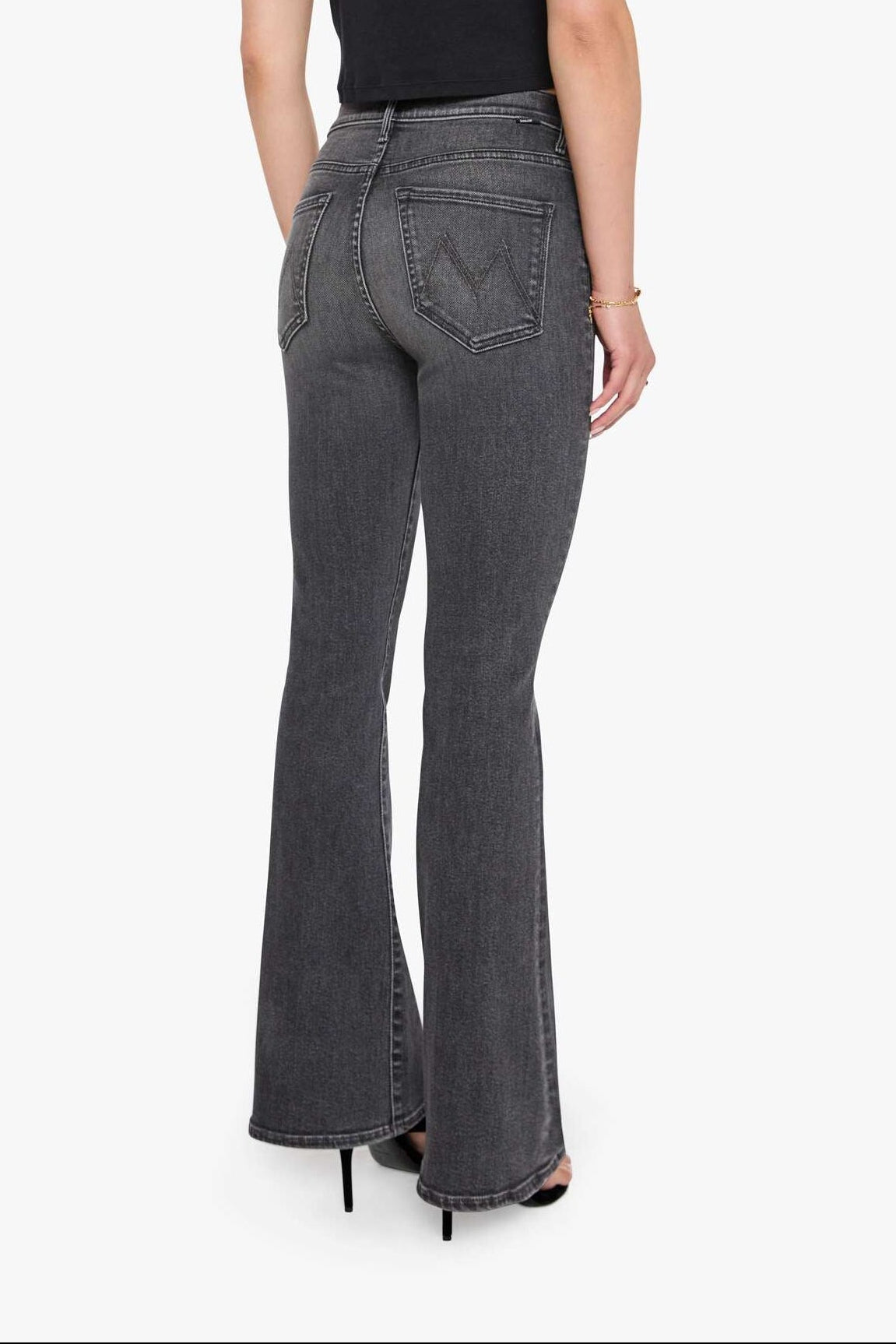 Woman wearing gray flared jeans and a black top on a white background