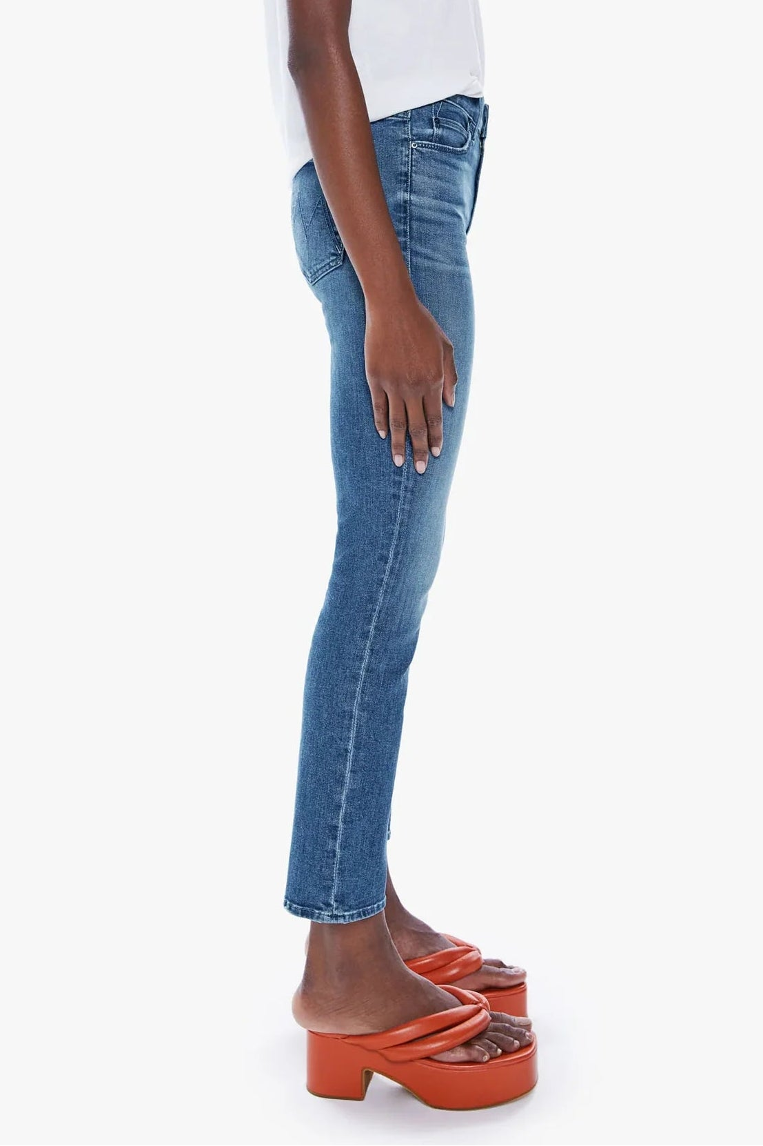 A model shown in profile wearing blue skinny jeans, a white short-sleeve t-shirt, and orange platform mule sandals against a plain light gray background.