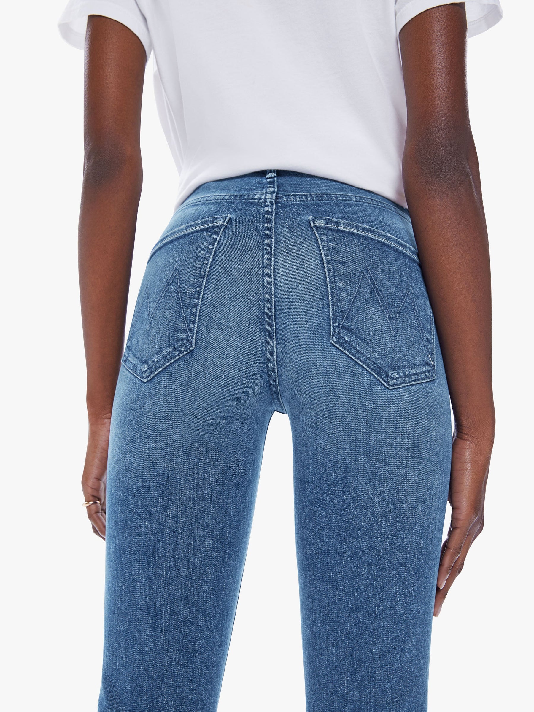 Rear view of a model wearing blue denim jeans and a white t-shirt against a plain white background.