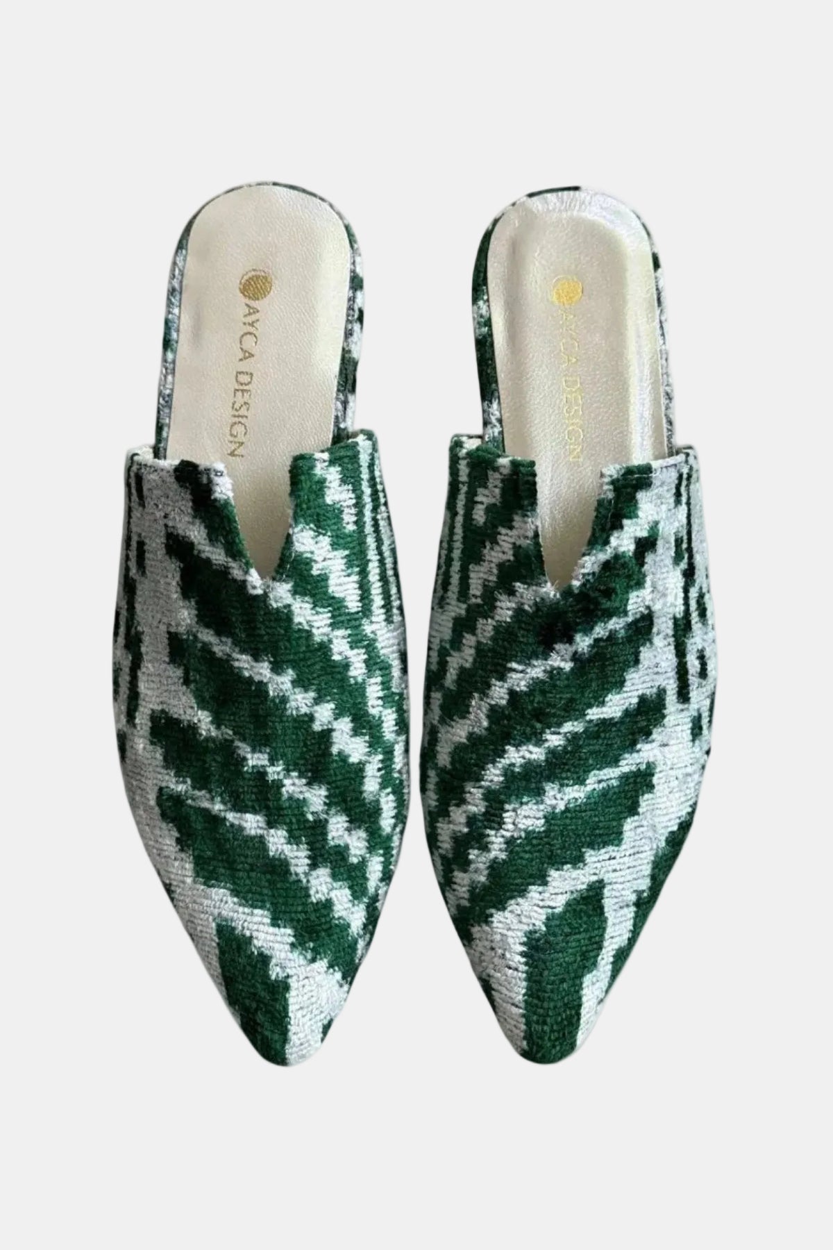 A pair of pointed-toe slip-on mule shoes with a green and white geometric woven pattern, shown from a top-down view on a white background. The insole features the brand name 'AVG DESIGN' in gold.