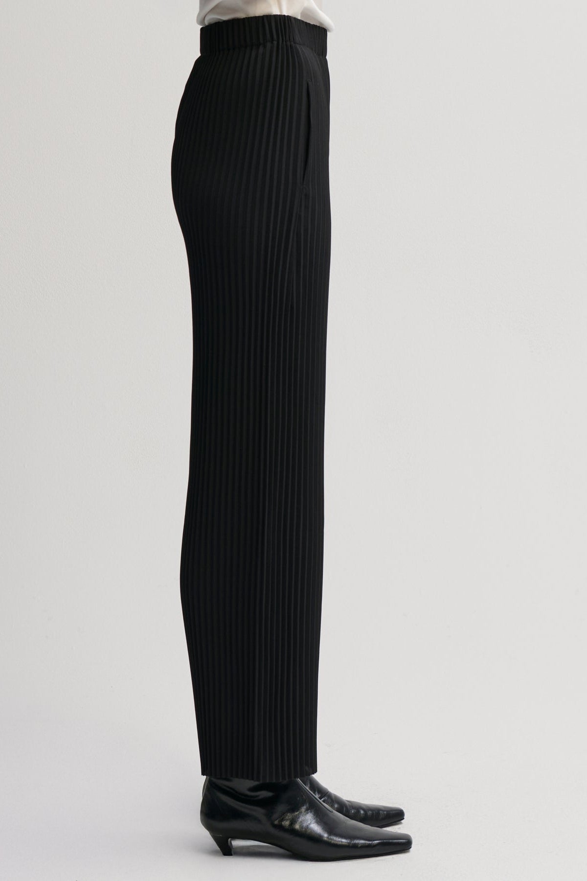 Black pleated wide-leg trousers shown on a model from the waist down, paired with black leather shoes against a light gray studio background.