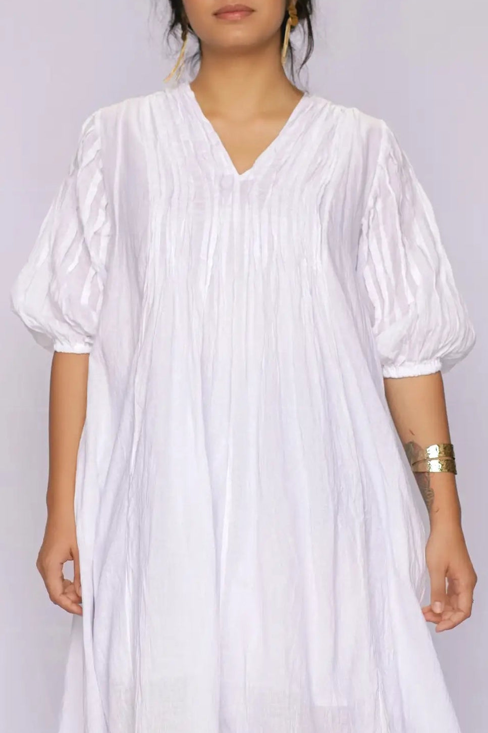 A woman wearing a white long-sleeve dress with a V-neck and gathered puff sleeves, standing against a plain light background.