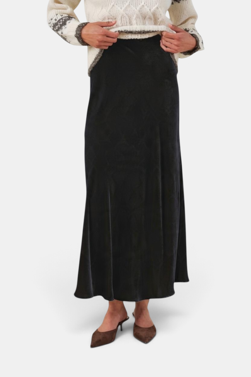 The Copper Shed Cadence black velvet maxi skirt with an A-line silhouette and elastic waist, worn with a knit sweater.