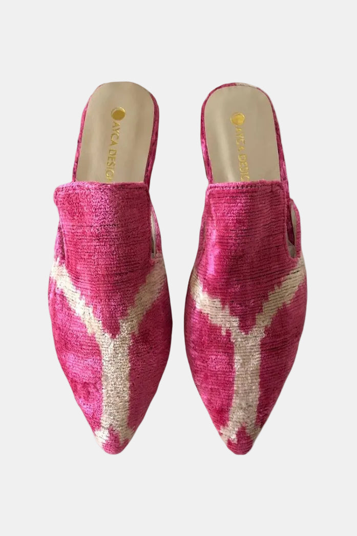 A pair of pointed-toe mule slippers in textured pink fabric with a cream ikat-style chevron pattern, shown from a top-down view on a white background. The brand name 'AKA ADELE' is visible on the insole.