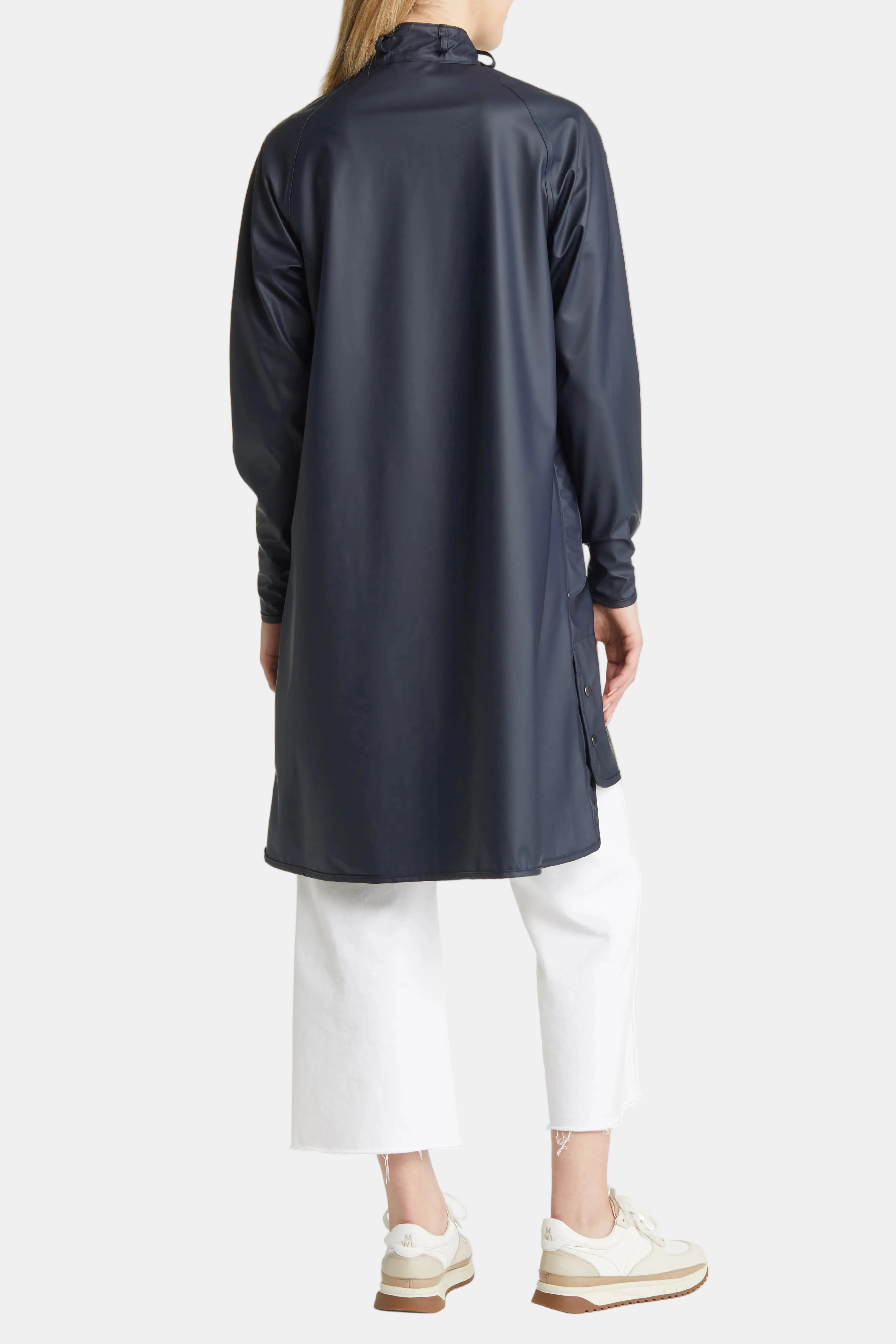A model shown from the back wearing a dark navy blue long-sleeve tunic or coat, paired with white cropped pants and beige sneakers, against a plain white background.