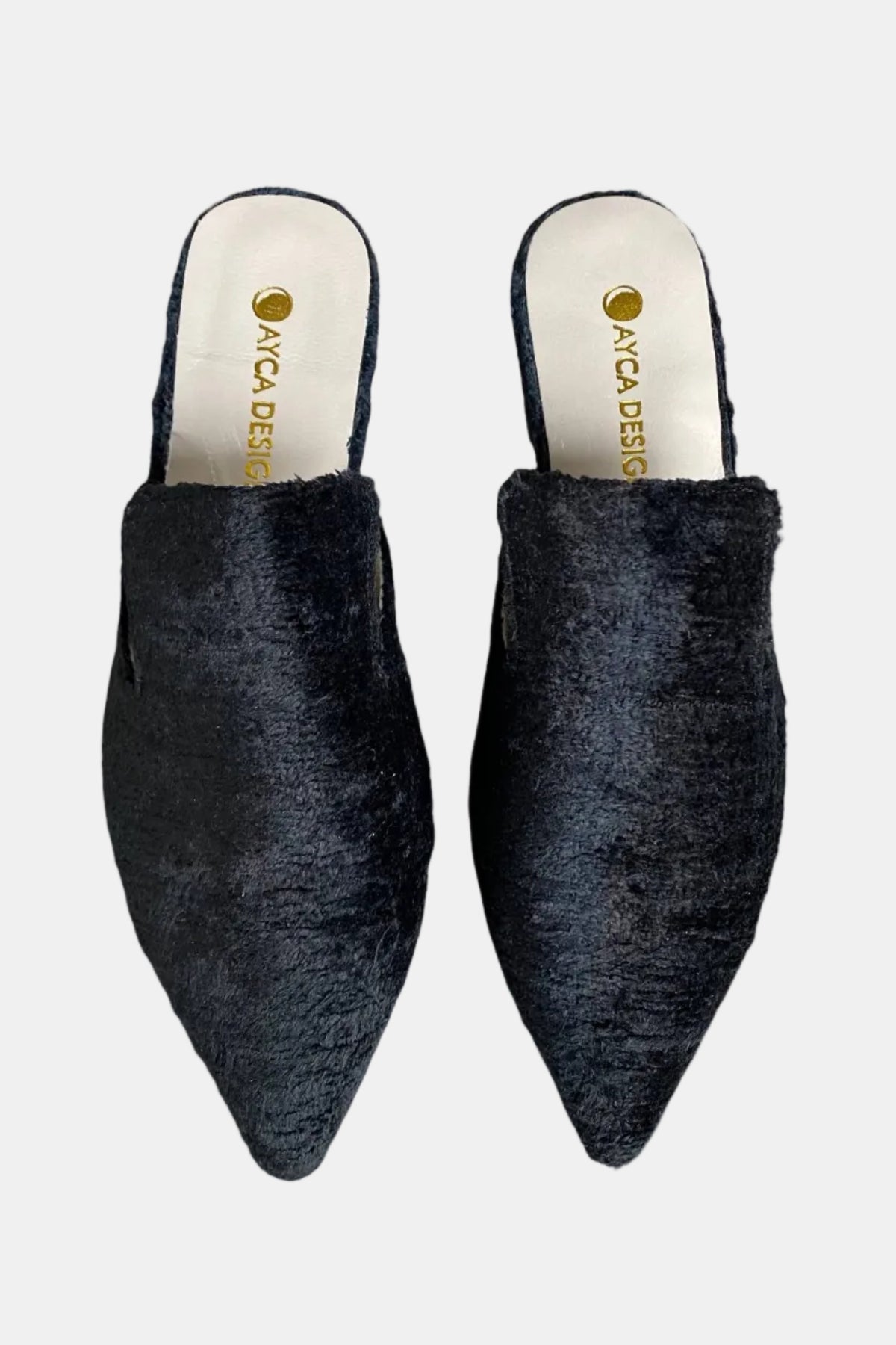 A pair of black fuzzy pointed-toe mule slippers with a cream insole and gold 'ANCA DESIGNS' branding, shown against a plain white background.