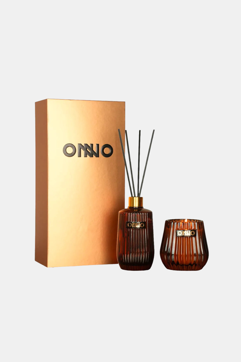 A reed diffuser set with a metallic gold box labeled 'ONNO', a ribbed amber glass bottle with reeds, and a matching amber glass diffuser cup on a light gray background.
