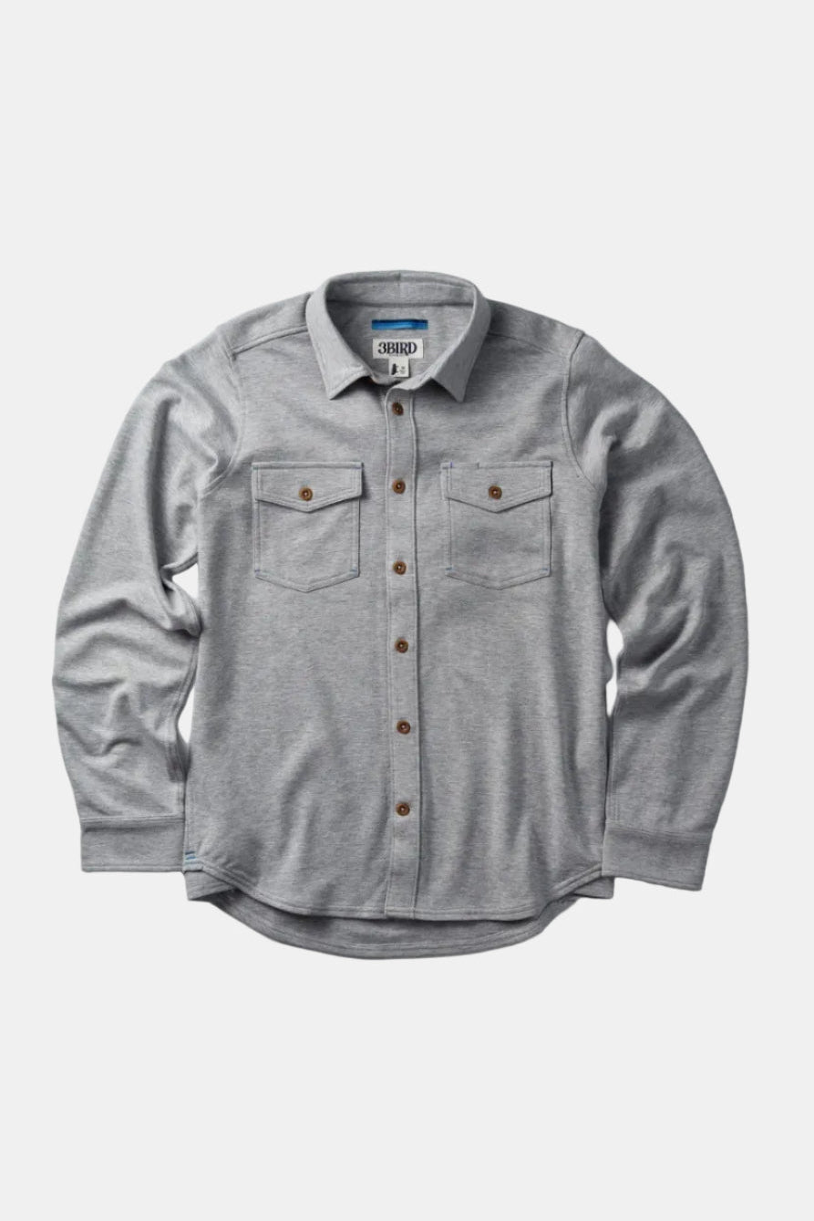 A light gray heather long-sleeve button-up shirt with two chest flap pockets and brown buttons, displayed flat against a light gray background.
