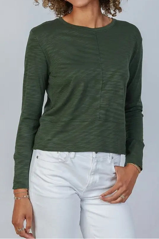 Woman wearing a green long-sleeve shirt and white pants against a plain background