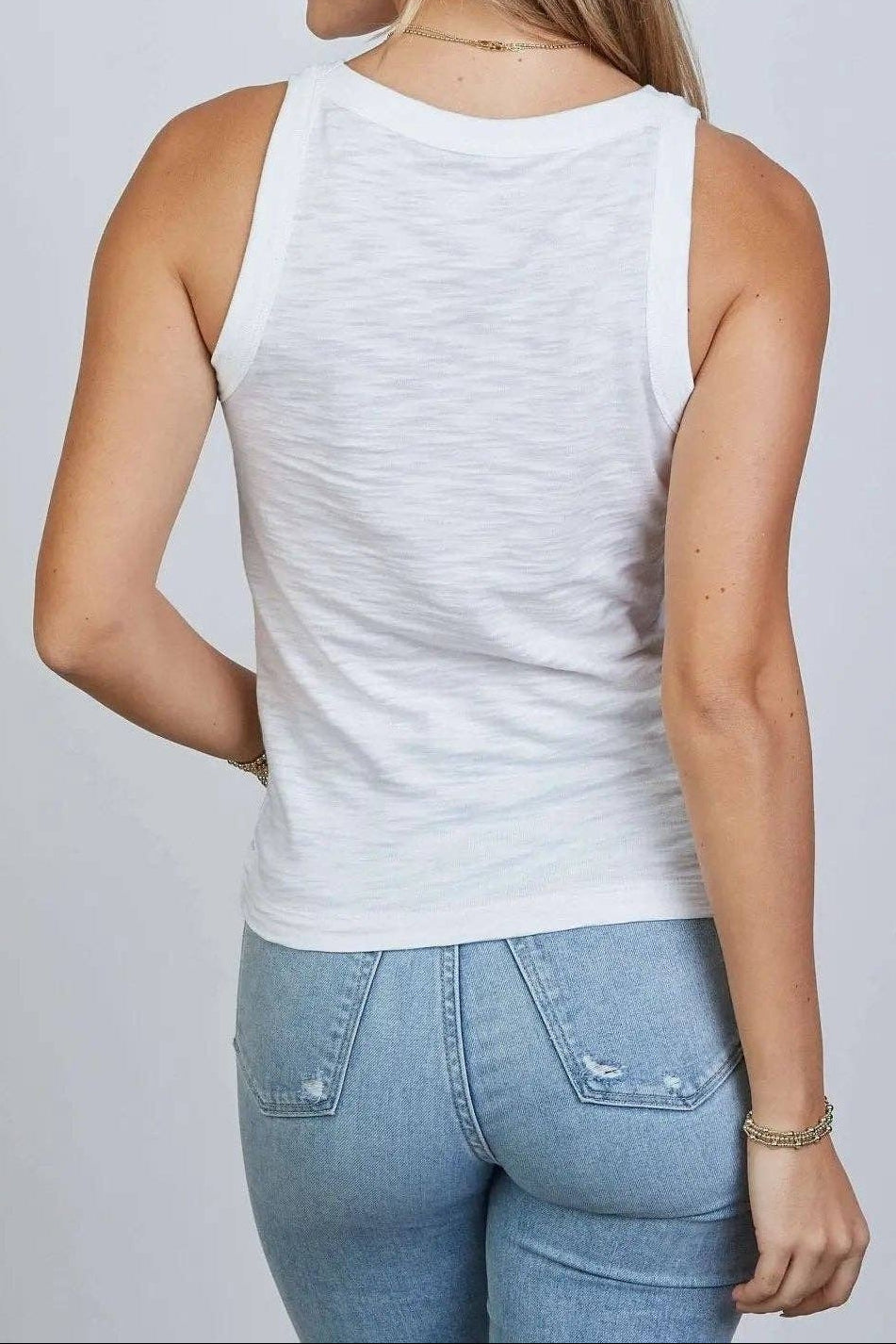 Woman wearing a white tank top and blue jeans on a plain background